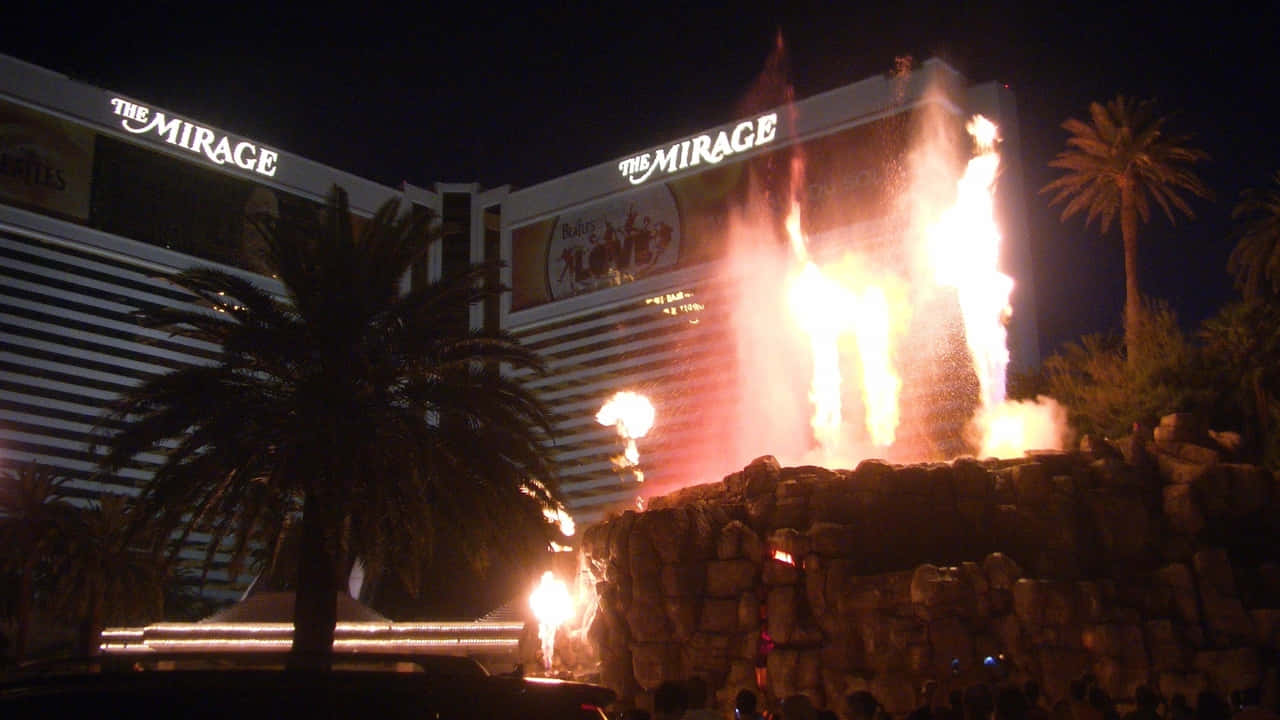 720p Las Vegas 桌布 壁紙 — 在米拉奇酒店前的岩石舞台上，一場耀眼的夜間火焰表演爆發，棕櫚樹在明亮的火焰中映出剪影。
