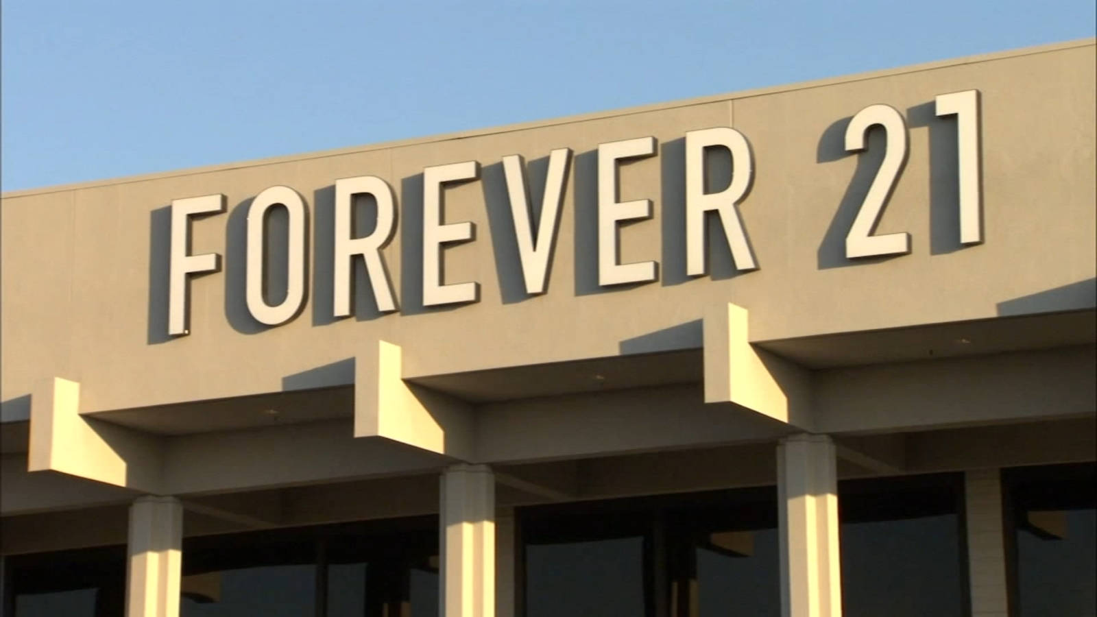 Forever 21 桌布 壁紙 — 在米色建築物上的Forever 21商店招牌特寫，背景是晴朗的藍天，溫暖的陽光投下陰影。