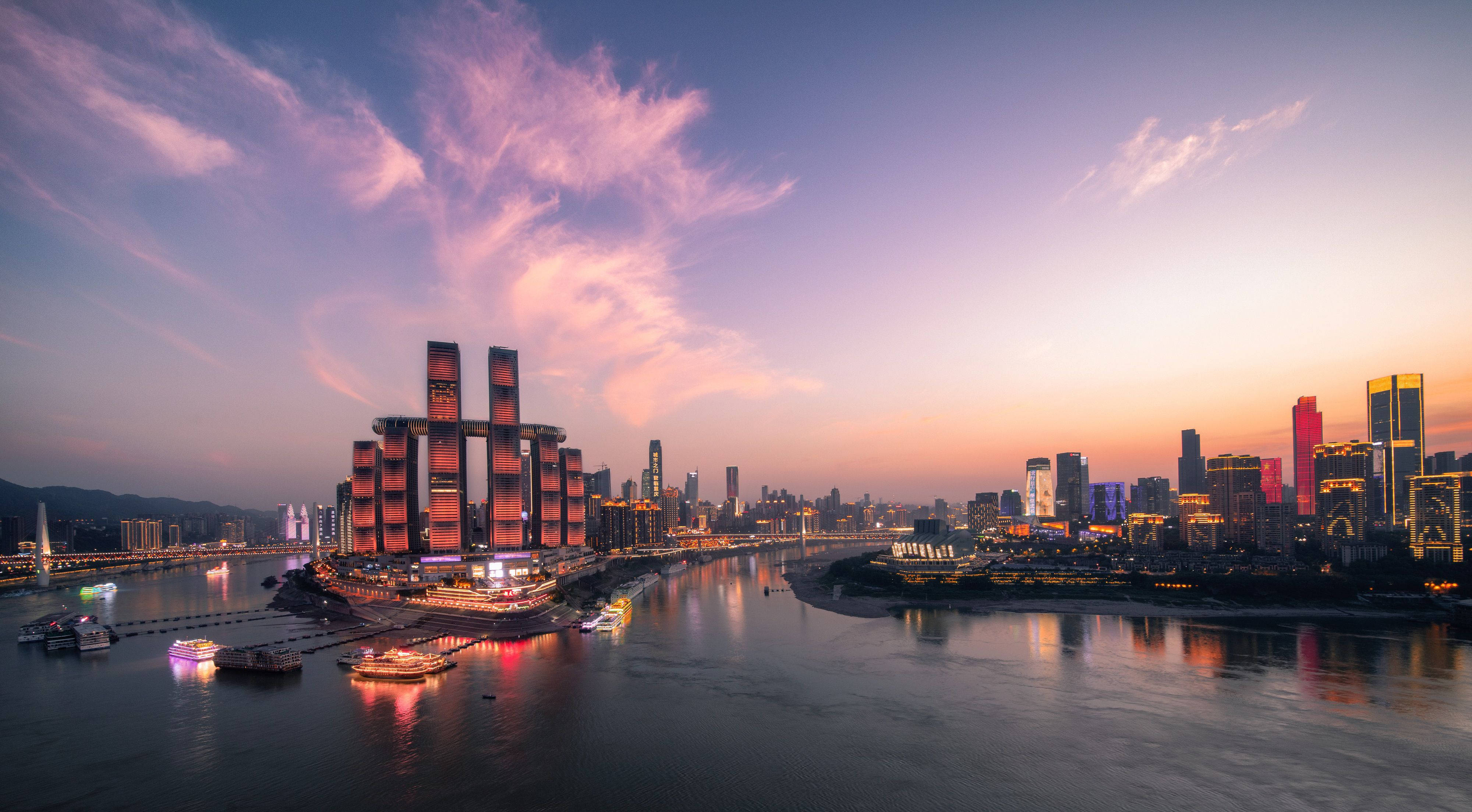 Chongqing 桌布 壁紙 — 在粉紅色和紫色雲彩下，夕陽時分充滿活力的城市天際線，閃爍的摩天大樓和反射河流上的船隻。