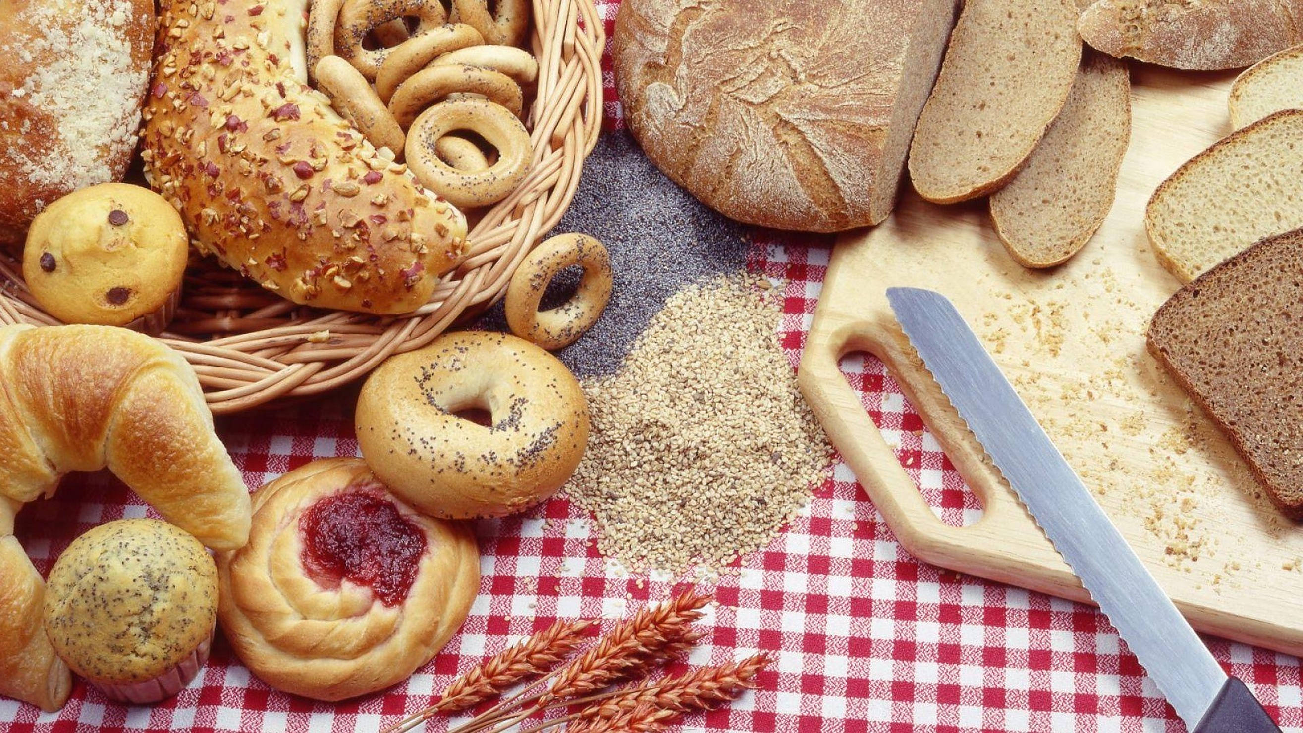 Bakery 桌布 壁紙 — 在紅色格子布上，鄉村風格地擺放著新鮮麵包、糕點和小麥，旁邊放著一把麵包刀。