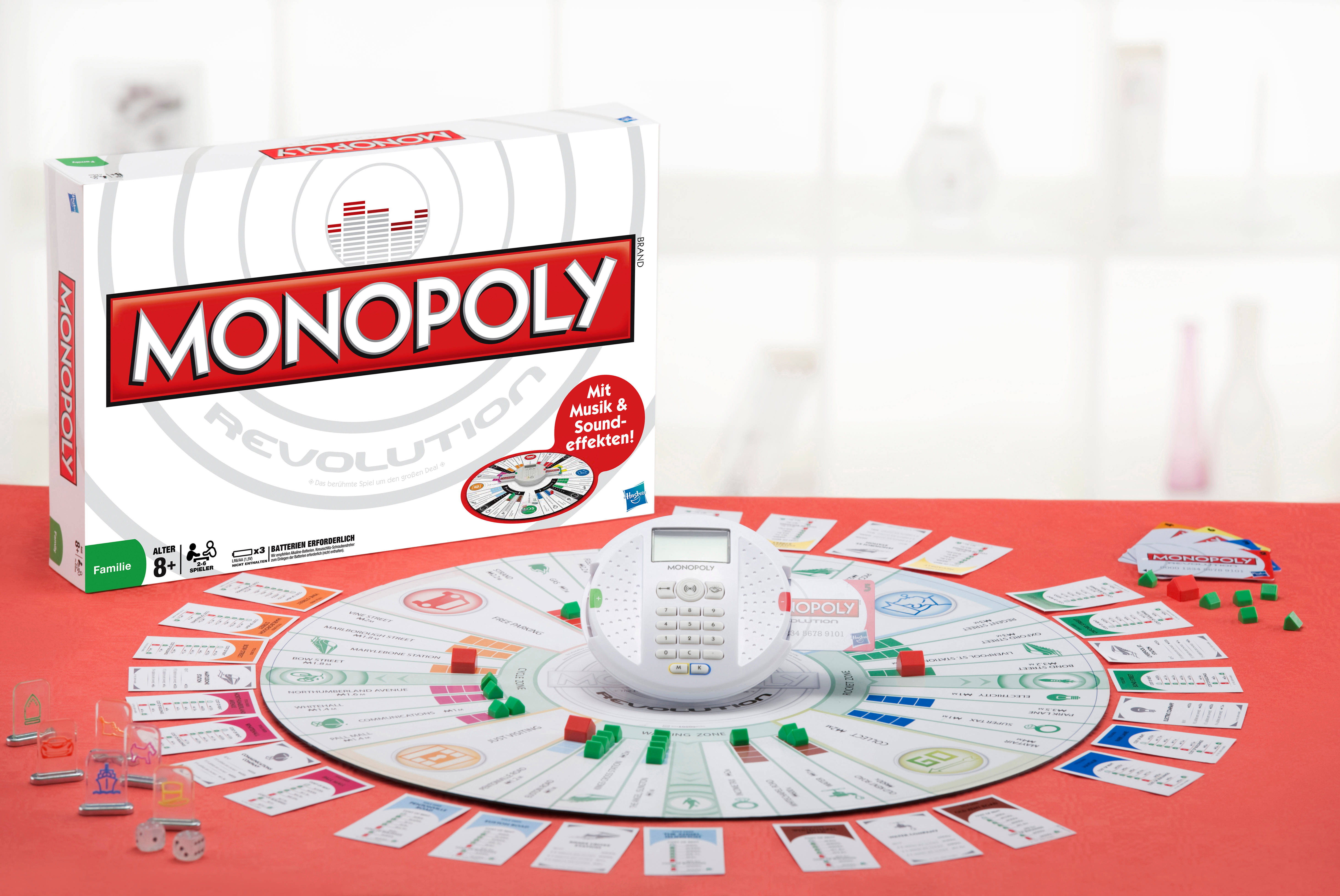 地產大亨 桌布 壁紙 — 在紅色桌子上設置的 Monopoly Revolution 棋盤遊戲，圓形棋盤周圍有卡牌、籌碼和數位計時器。