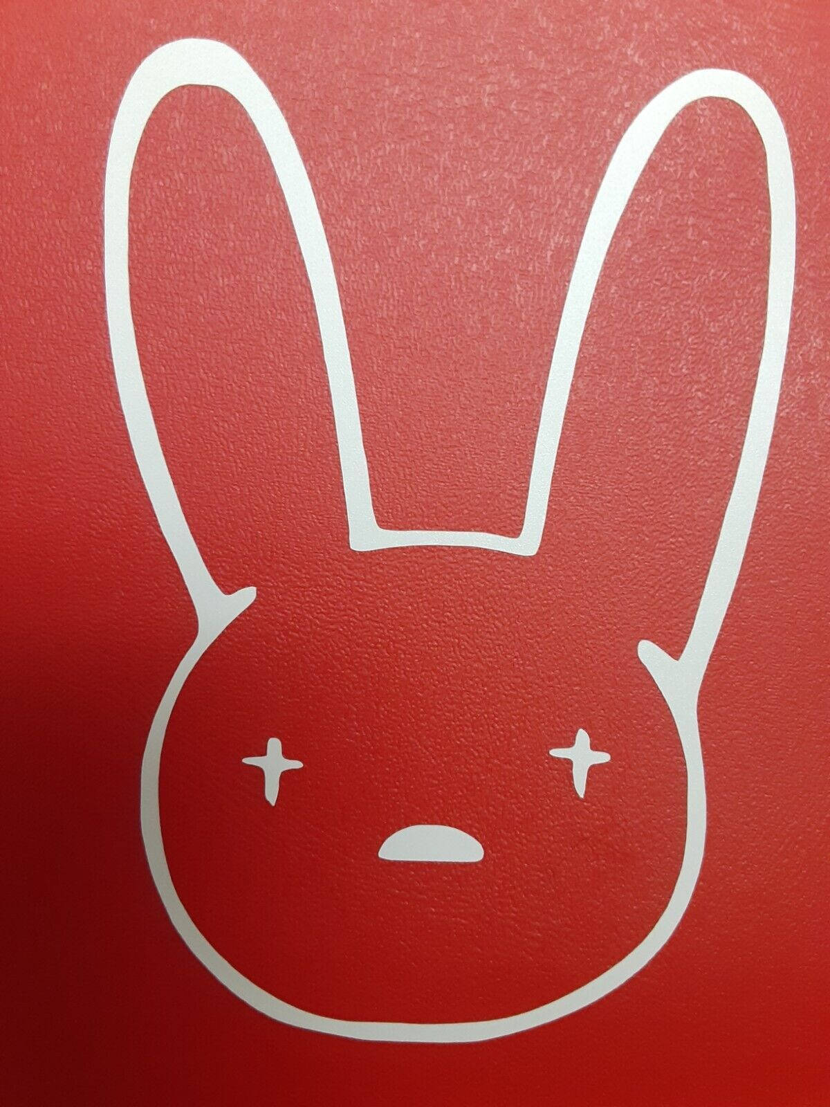 Bad Bunny Logo 桌布 壁紙 — 在紋理紅色背景上，一個極簡主義的白色線條繪畫，描繪一個有交叉眼睛和小嘴巴的兔子臉。