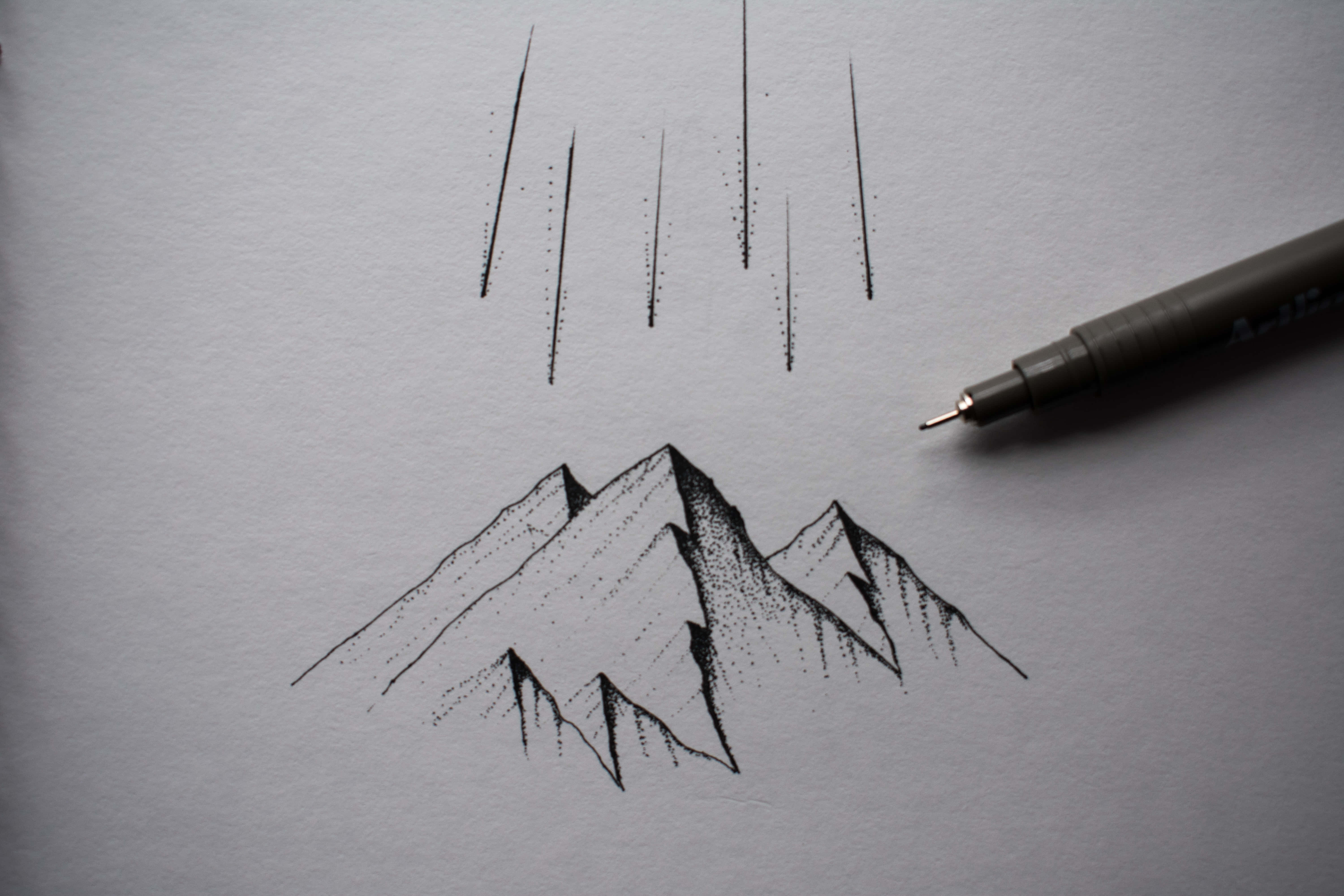 Drawing 桌布 壁紙 — 在紋理紙上以黑色墨水繪製的極簡山脈草圖，旁邊放著一支筆。