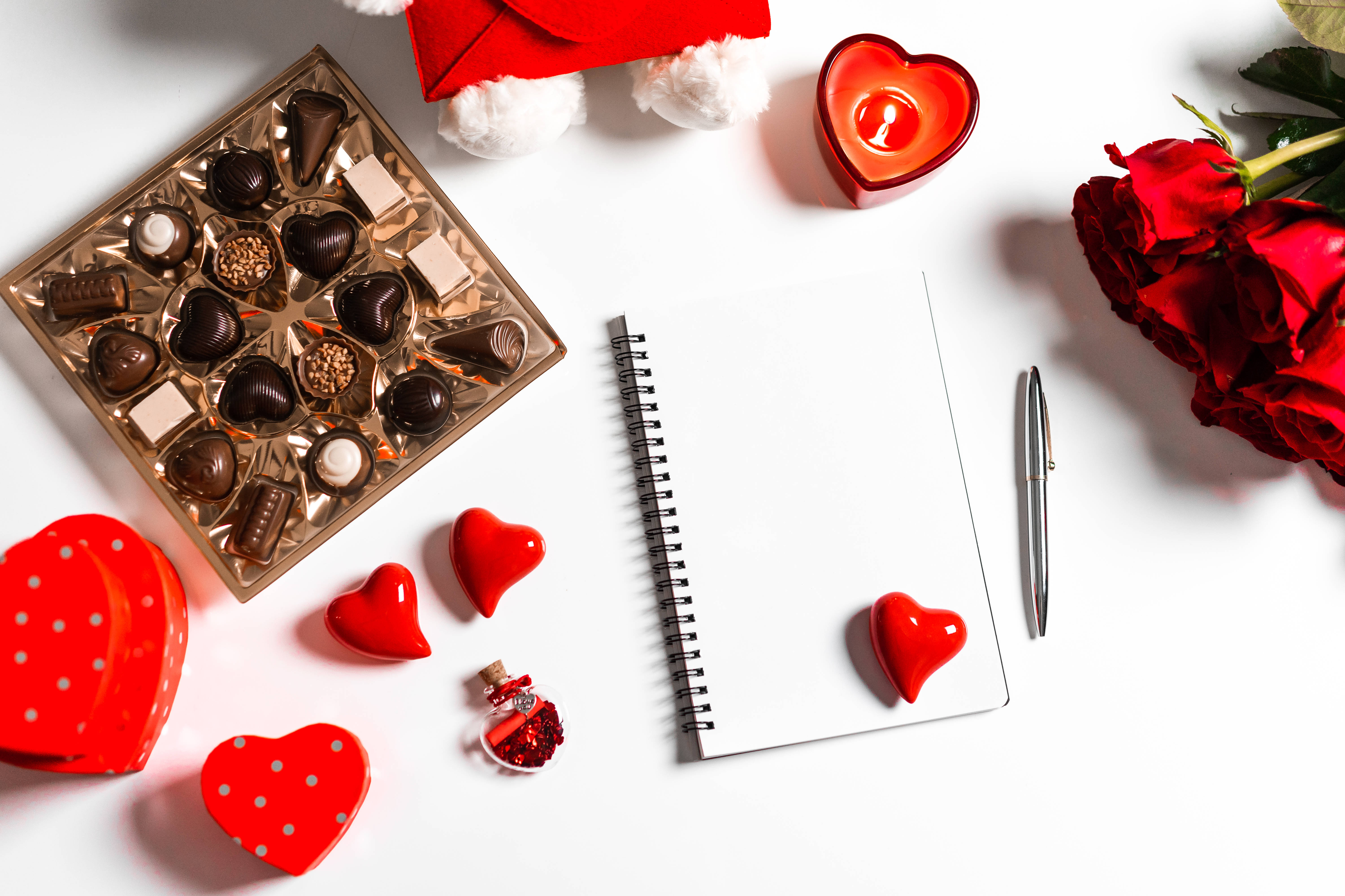 I Love You Aesthetic 桌布 壁紙 — 在純白表面上，紅玫瑰、巧克力、心形蠟燭和筆記本平鋪擺放。
