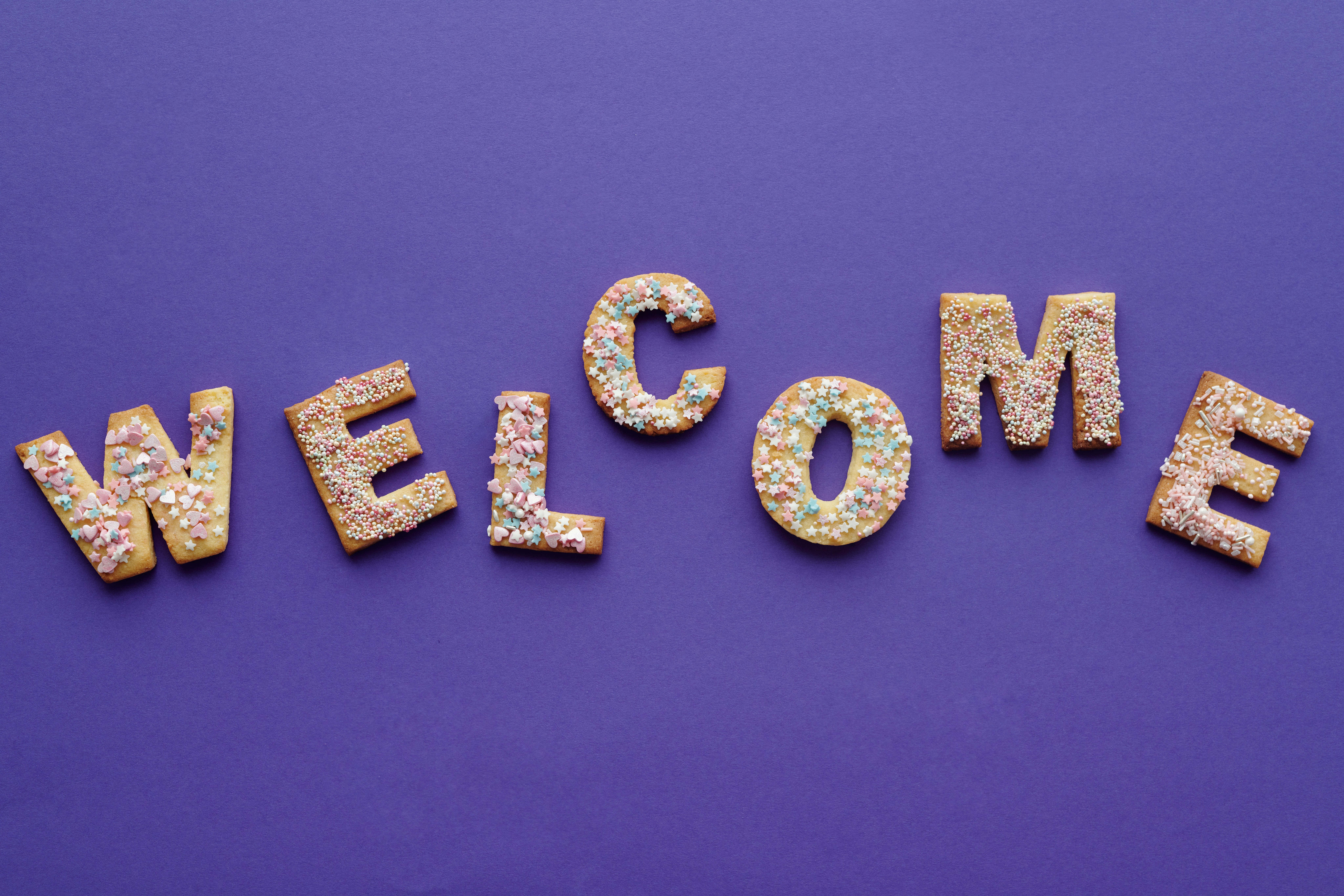 Welcome 桌布 壁紙 — 在純紫色背景上，用色彩繽紛的糖霜餅乾拼出「WELCOME」一詞。