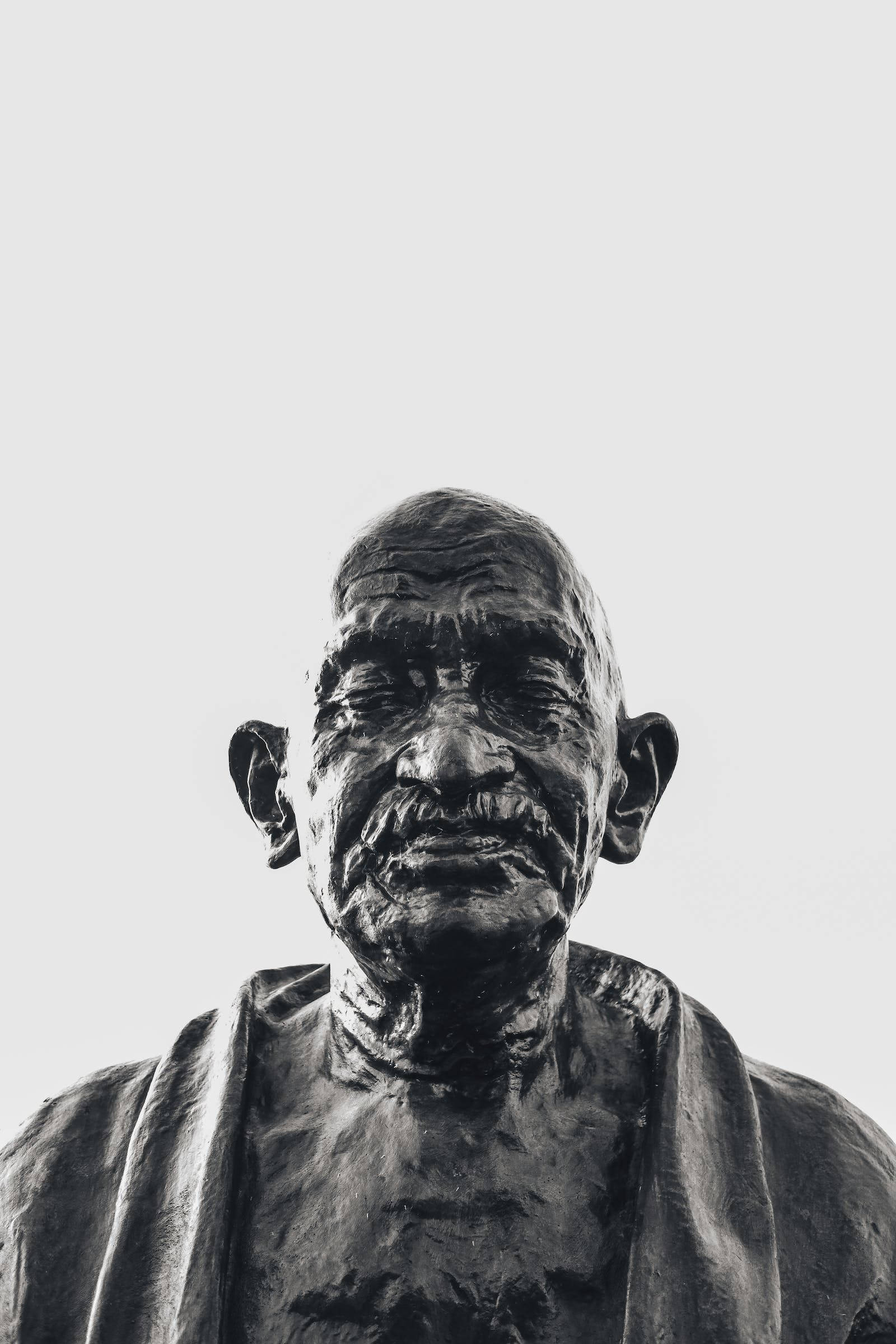 Mahatma Gandhi 桌布 壁紙 — 在純色淺色背景上，一張風化的聖雄甘地銅像的清晰黑白特寫。