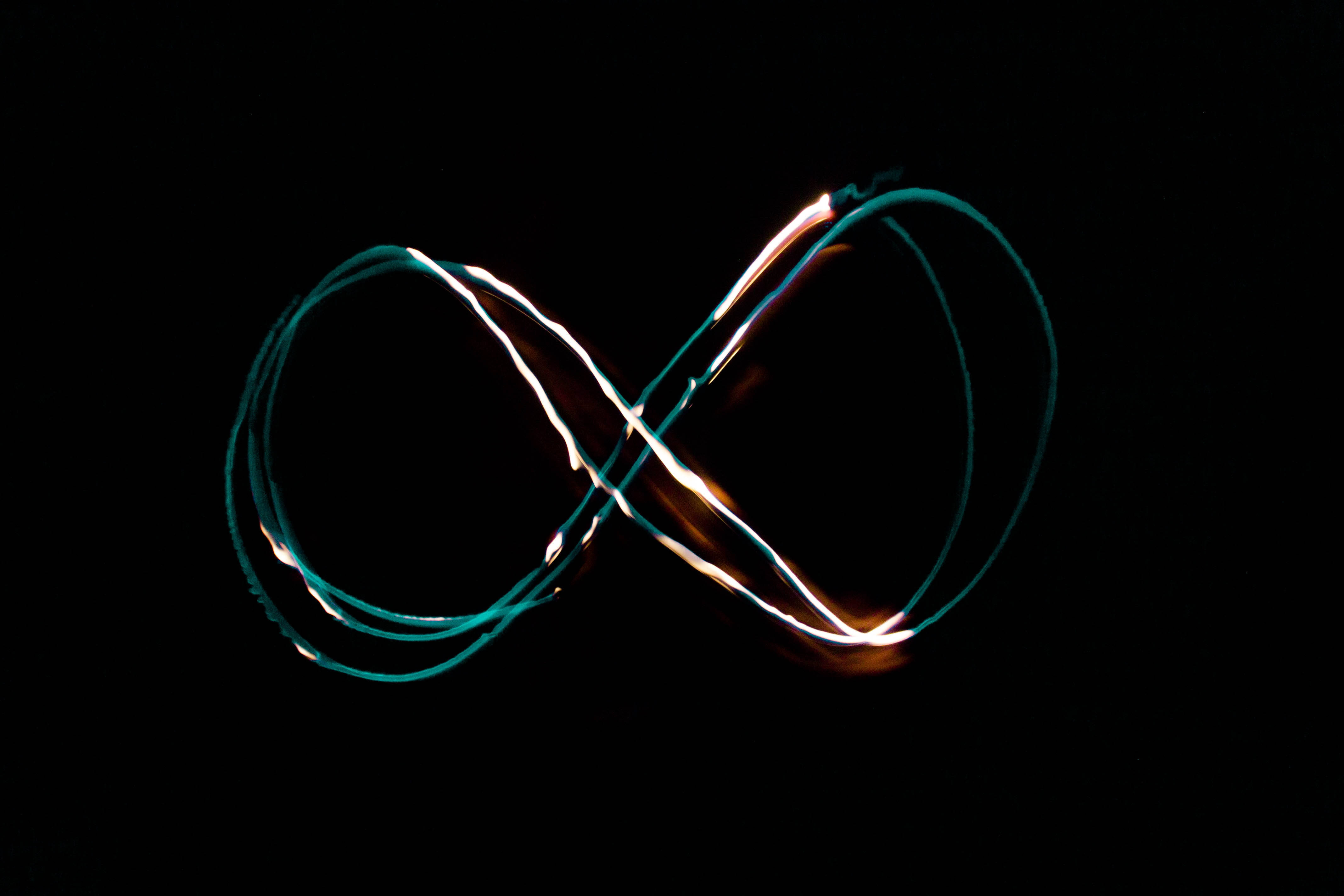 Infinity Symbol 桌布 壁紙 — 在純黑背景上，由青綠色和金色光跡形成的發光無限符號。