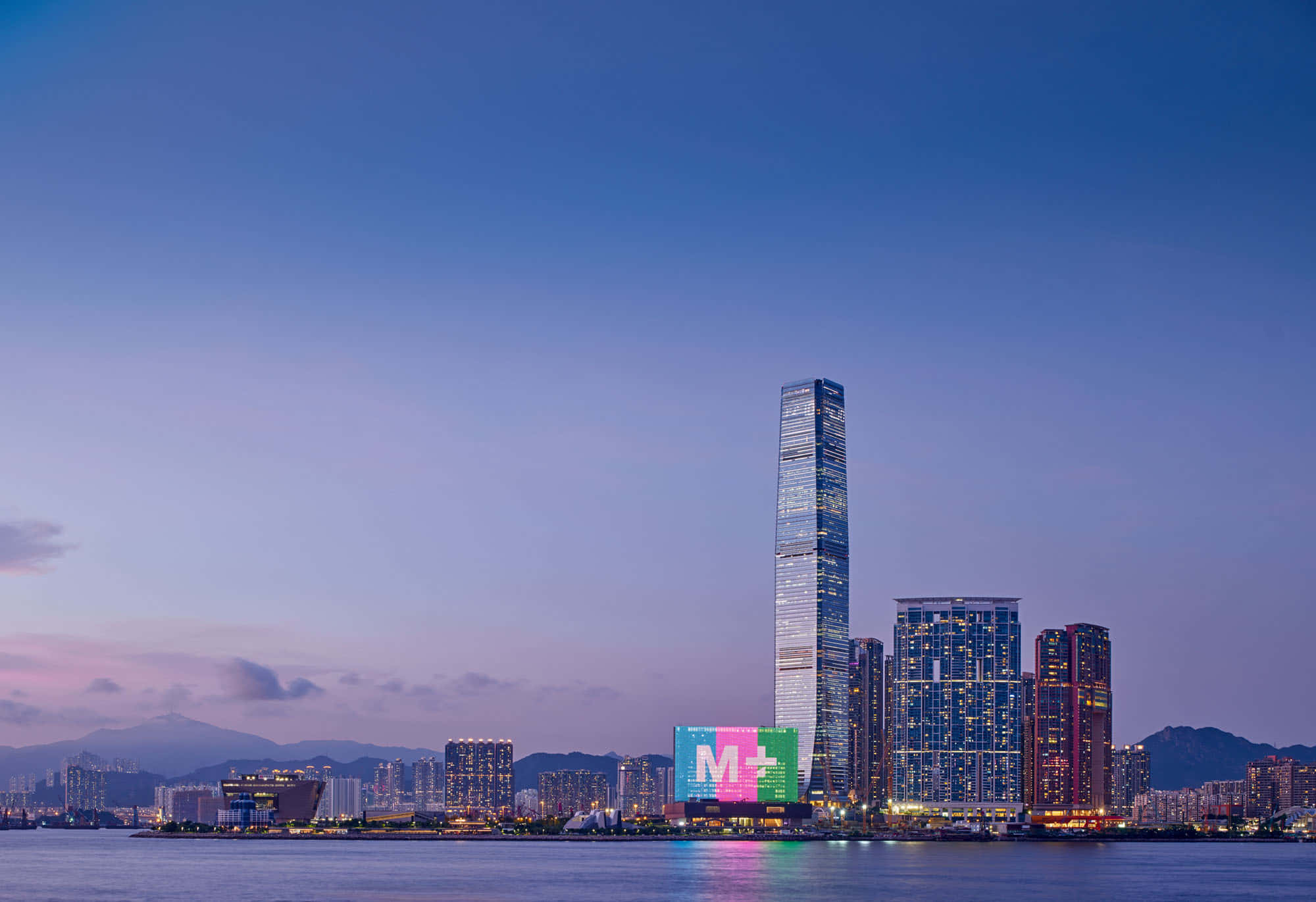 香港 桌布 壁紙 — 在紫色天空下，高聳的摩天大樓倒映在平靜水面上，令人驚嘆的黃昏城市景觀。