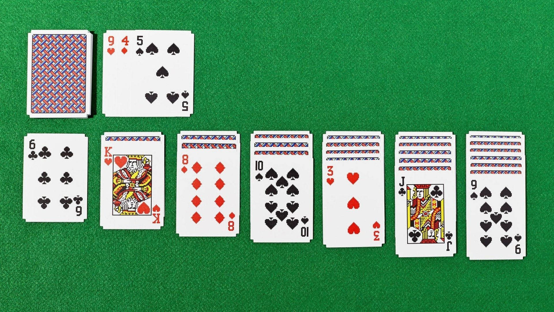 Solitaire 桌布 壁紙 — 在綠色絨面表面上散開的撲克牌，顯示遊戲設置中的各種花色和點數。