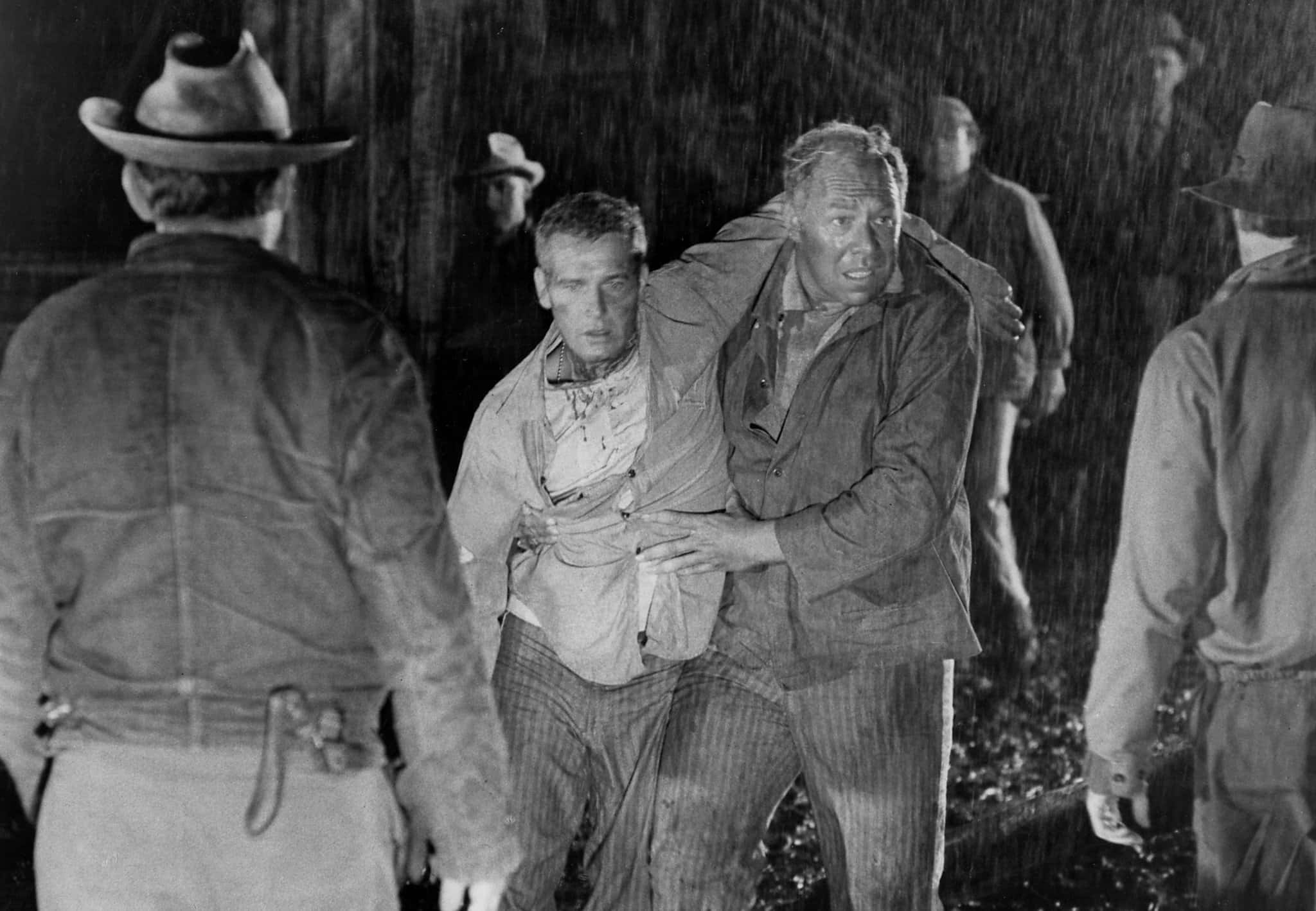 George Kennedy 桌布 壁紙 — 在緊張的黑白西部場景中，一名男子被另一名男子拖著穿過大雨。