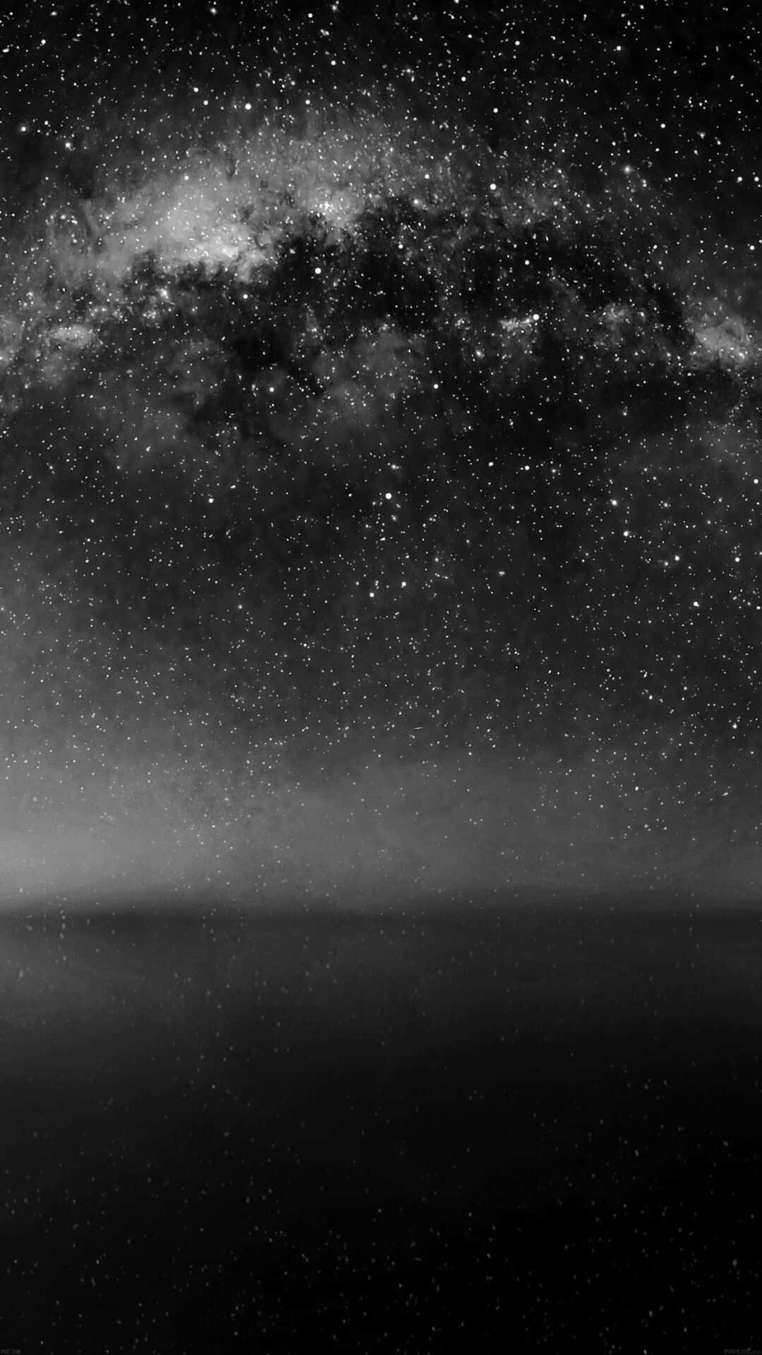 Dark Sky 桌布 壁紙 — 在繁星滿天的天空下，銀河系橫跨霧氣瀰漫的地平線，呈現出令人驚嘆的黑白景觀。
