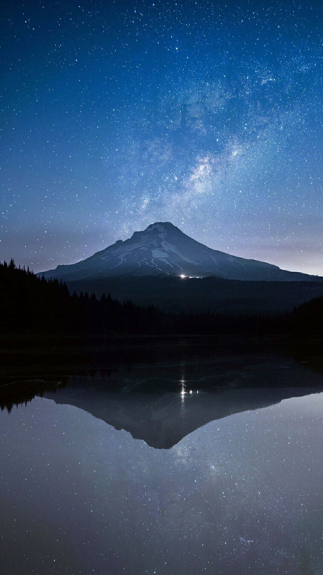 桌布 壁紙 — 在繁星點點的夜空下，一座積雪的山峰將銀河完美地倒映在平靜的湖面上。