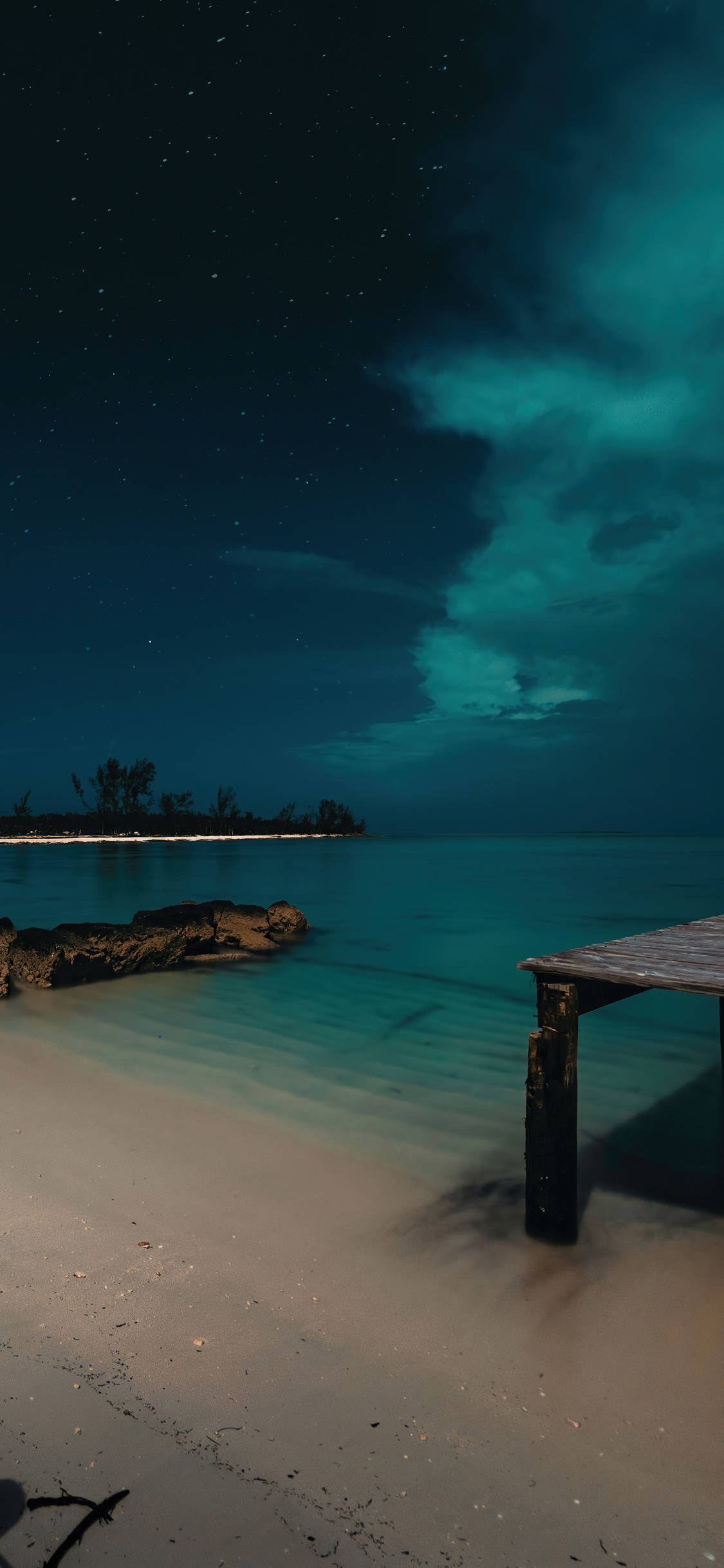 Nassau Bahamas 桌布 壁紙 — 在繁星點點的夜空下，一條木製碼頭延伸至碧綠色的海水，伴隨著發光的青綠色雲彩。