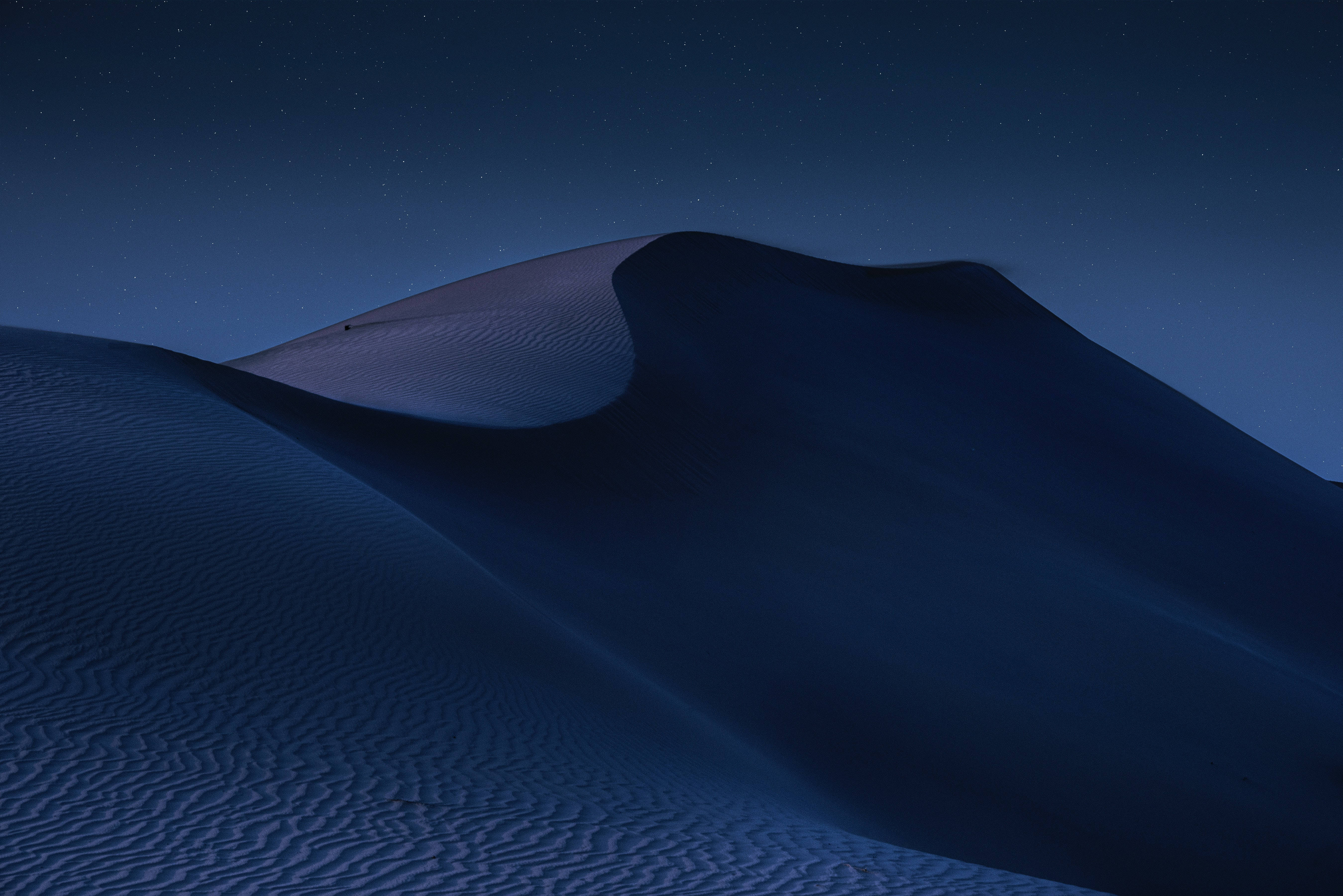 Dark 4K 桌布 壁紙 — 在繁星點點的夜空下，柔和的藍色燈光和紋理沙子的寧靜沙漠沙丘。