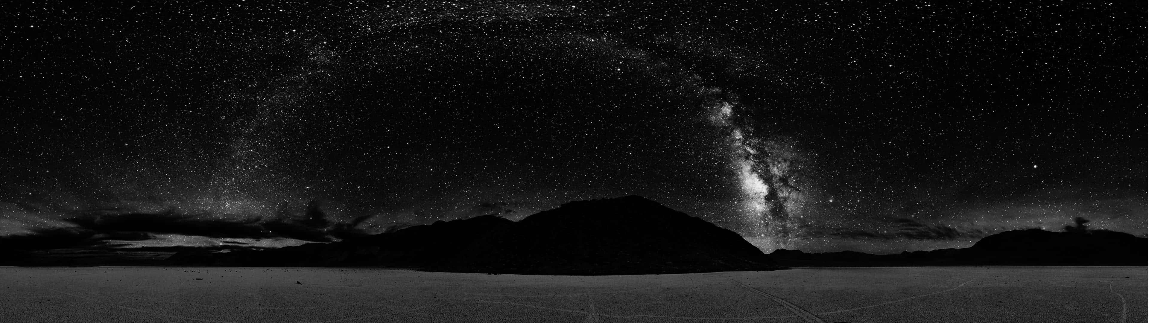 桌布 壁紙 — 在繁星點點的夜空下，銀河橫跨在剪影般的山脈之上，令人嘆為觀止的黑白全景。