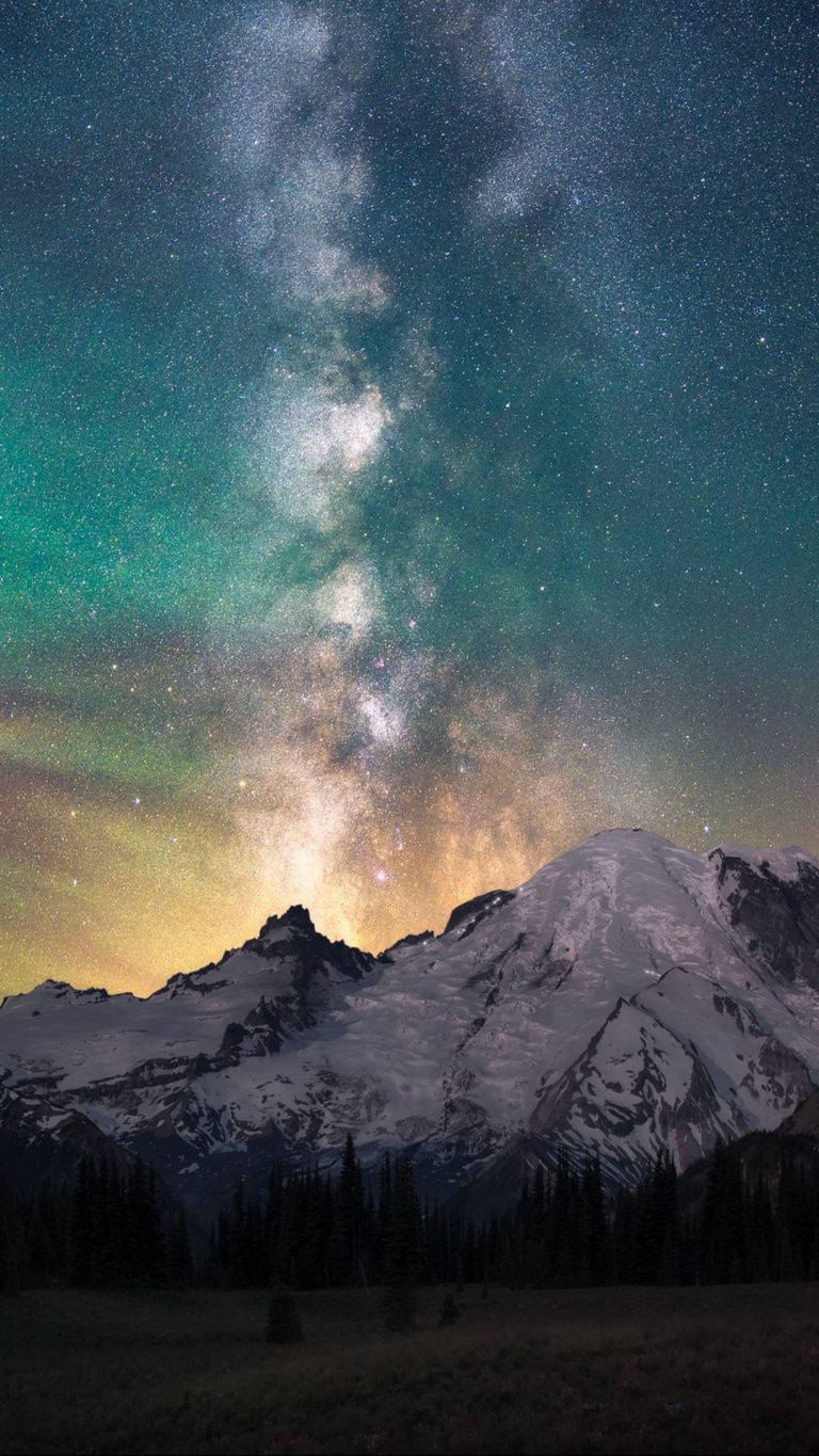 Honor 桌布 壁紙 — 在繁星點點的夜空中，一條雪覆蓋的山脈下方，有條生動的綠色和金色銀河系劃過天際。
