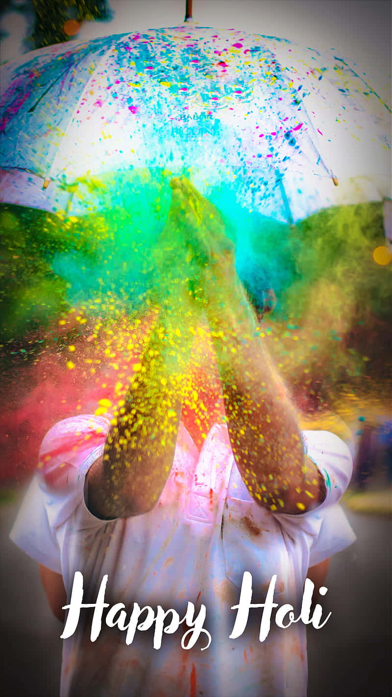 Holi 桌布 壁紙 — 在色彩繽紛的雨傘下，一個人在灑紅節期間歡快地將鮮豔的粉末拋向空中。