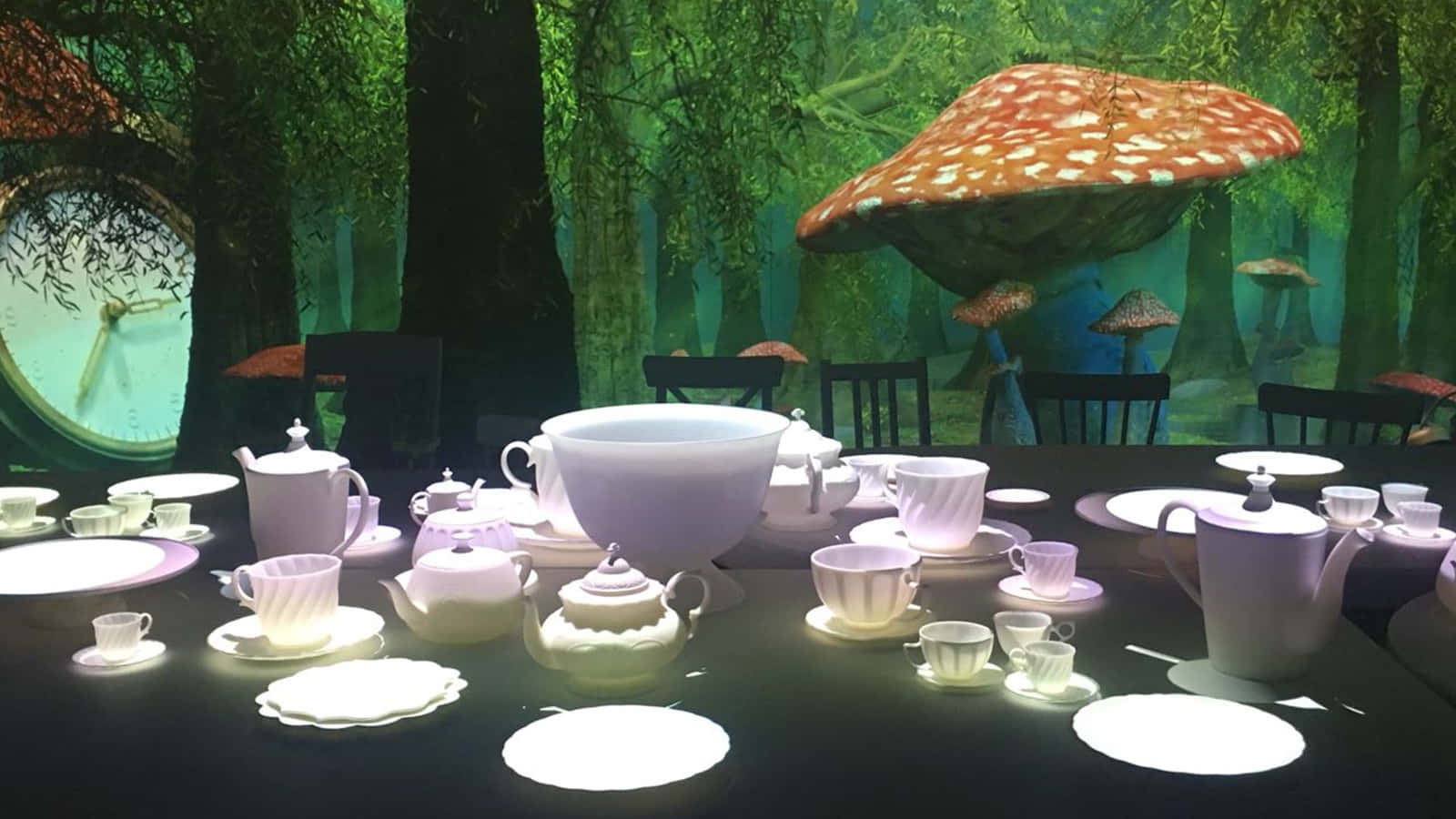 Tea Party 桌布 壁紙 — 在茂密的綠色森林中舉行的一場超現實茶會，有巨大的蘑菇和嵌入樹中的巨大時鐘。