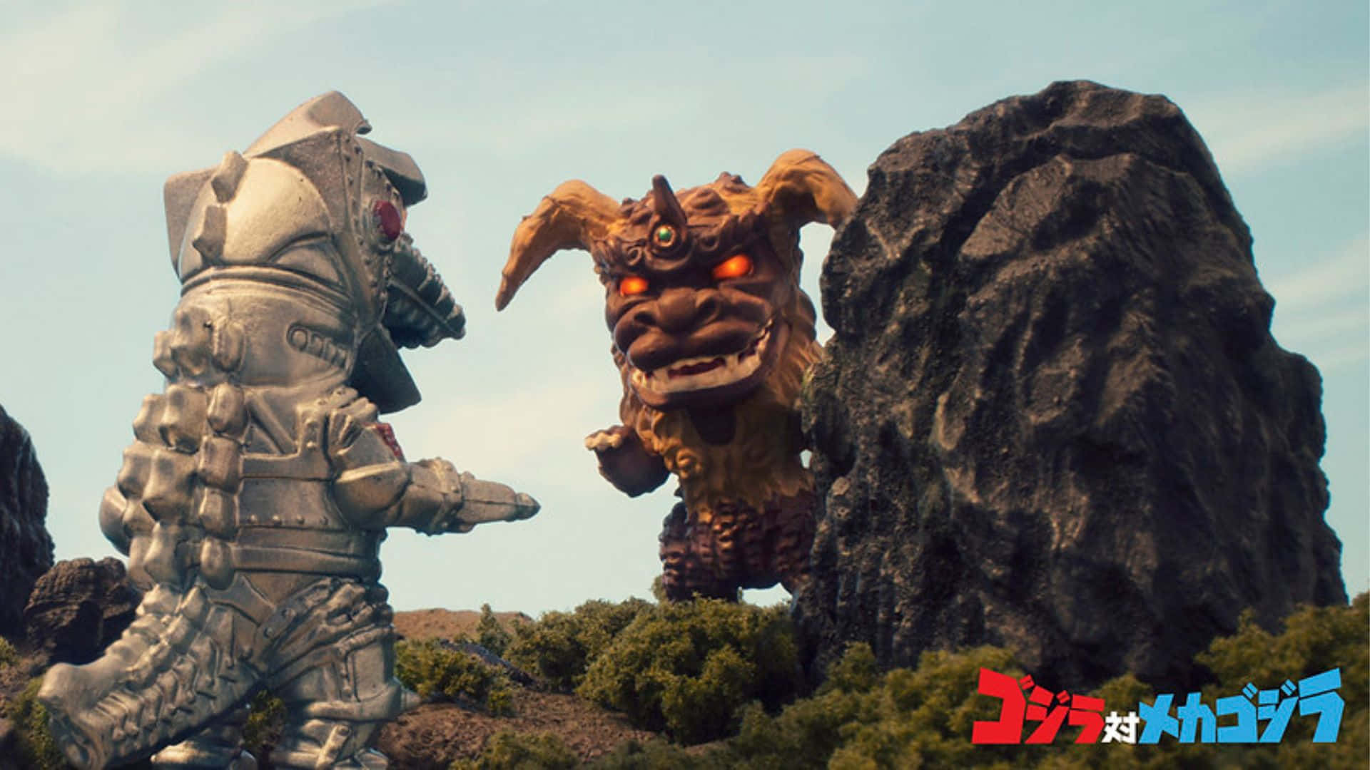 Godzilla Vs King Caesar 桌布 壁紙 — 在蒼白天空下，一個巨大的銀色機器人在岩石地形和綠色灌木叢中，面對一隻擁有發光紅眼的怪獸級棕色哥吉拉。