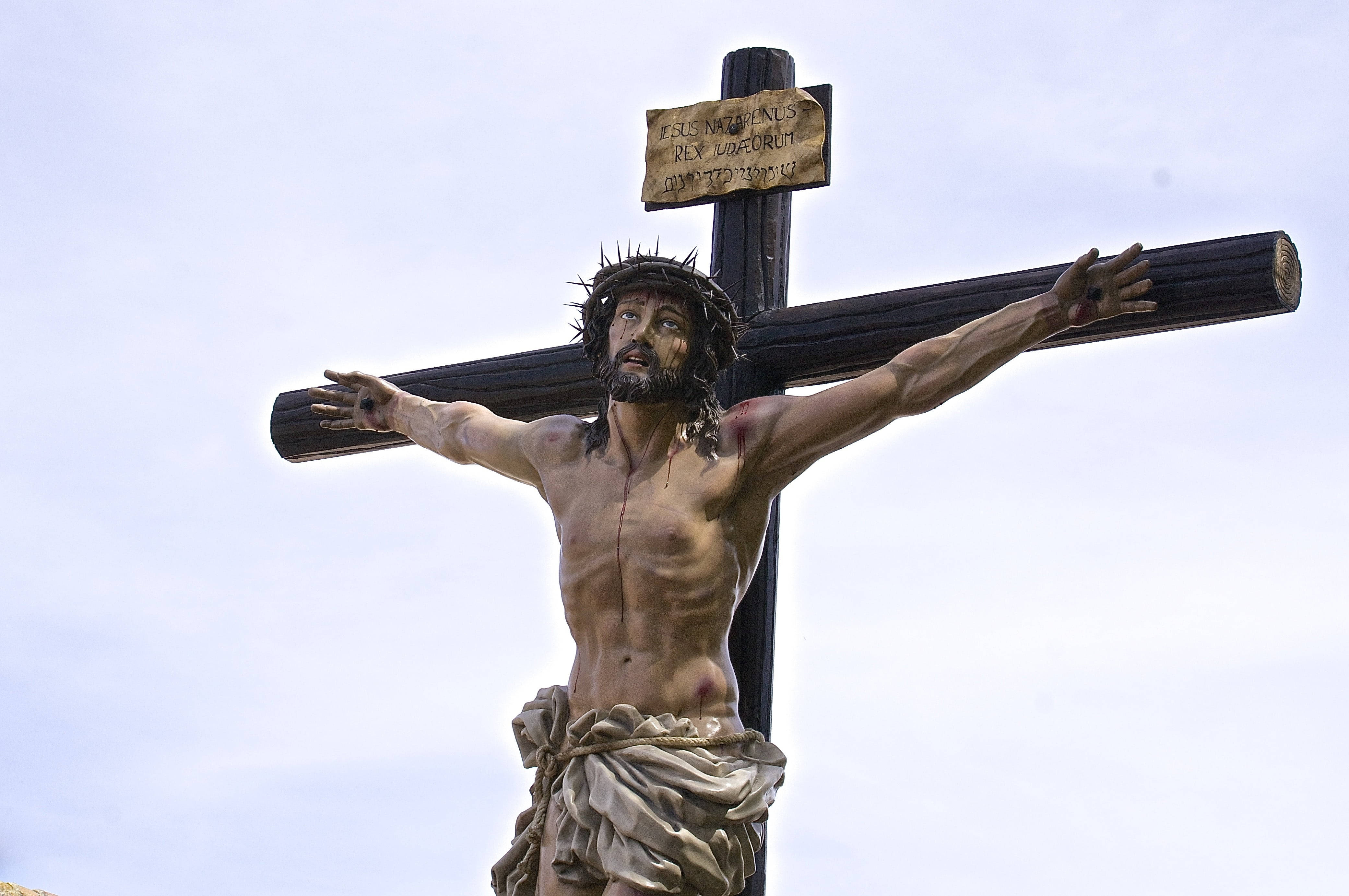 Christ 桌布 壁紙 — 在蒼白天空下，一個詳細的耶穌基督雕像釘在木製十字架上，附有拉丁文銘牌。