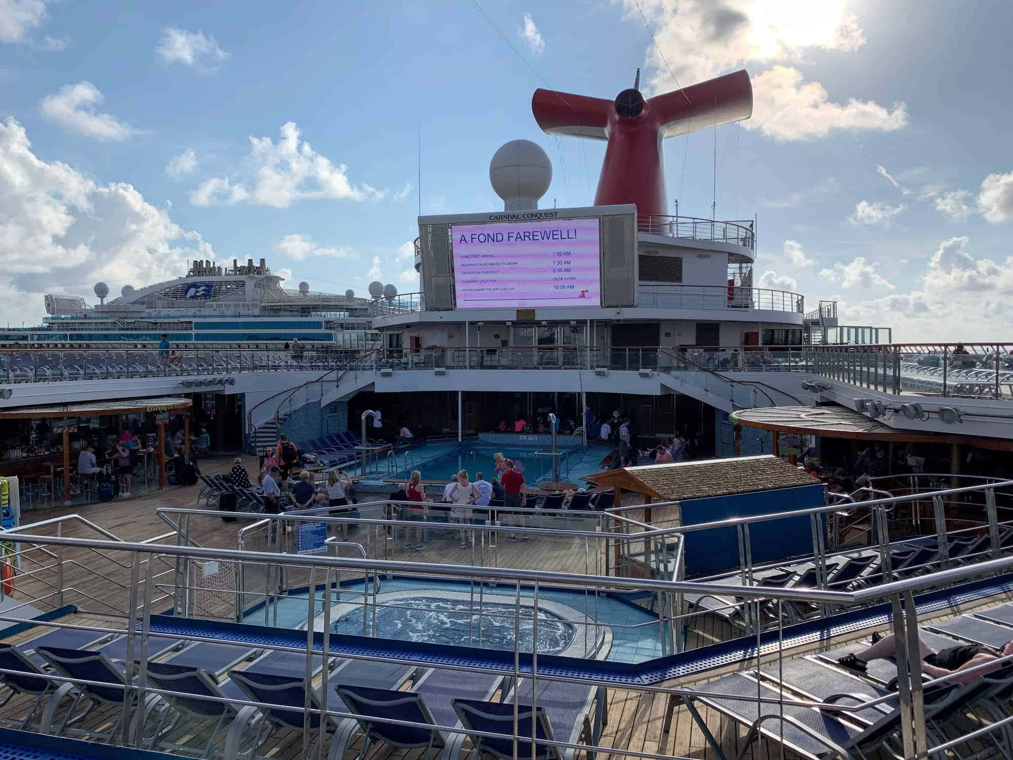 Carnival Conquest 桌布 壁紙 — 在藍天下，Carnival Conquest 郵輪甲板上的一個陽光明媚的日子，設有游泳池、躺椅和告別標誌。
