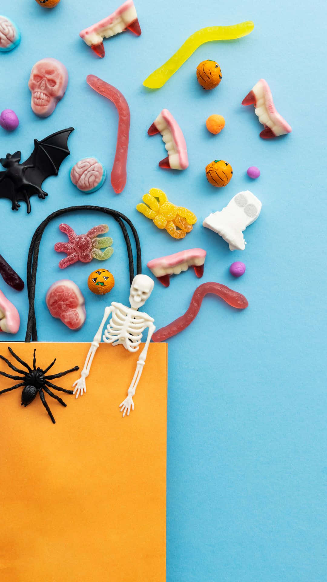 Trick Or Treat Bags 桌布 壁紙 — 在藍色和橙色背景上，包括頭骨、蝙蝠和骷髏在內的萬聖節糖果和玩具的平鋪佈局。