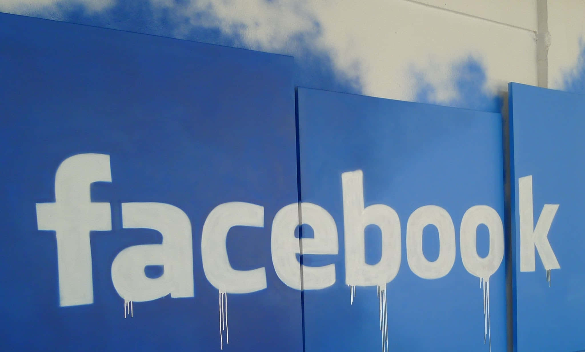 Facebook 桌布 壁紙 — 在藍色面板上以滴落白色字母繪製的塗鴉風格Facebook標誌，背景為多雲天空。