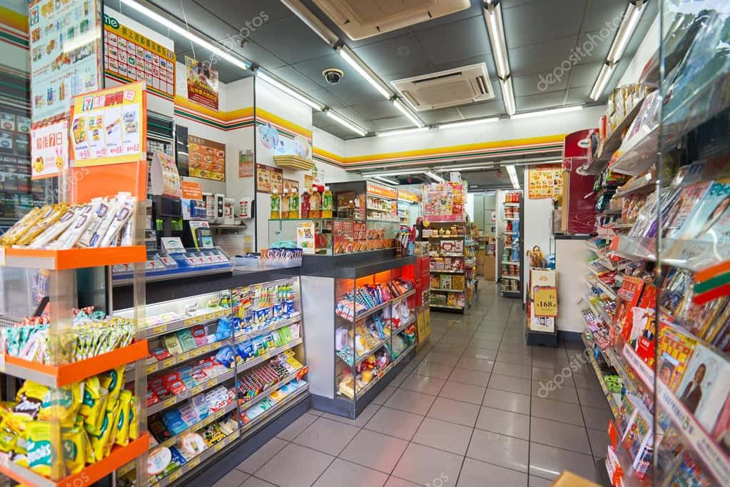7-ELEVEN 桌布 壁紙 — 在螢光燈下，一條明亮照明的便利商店通道，擺滿了色彩繽紛的零食和產品。