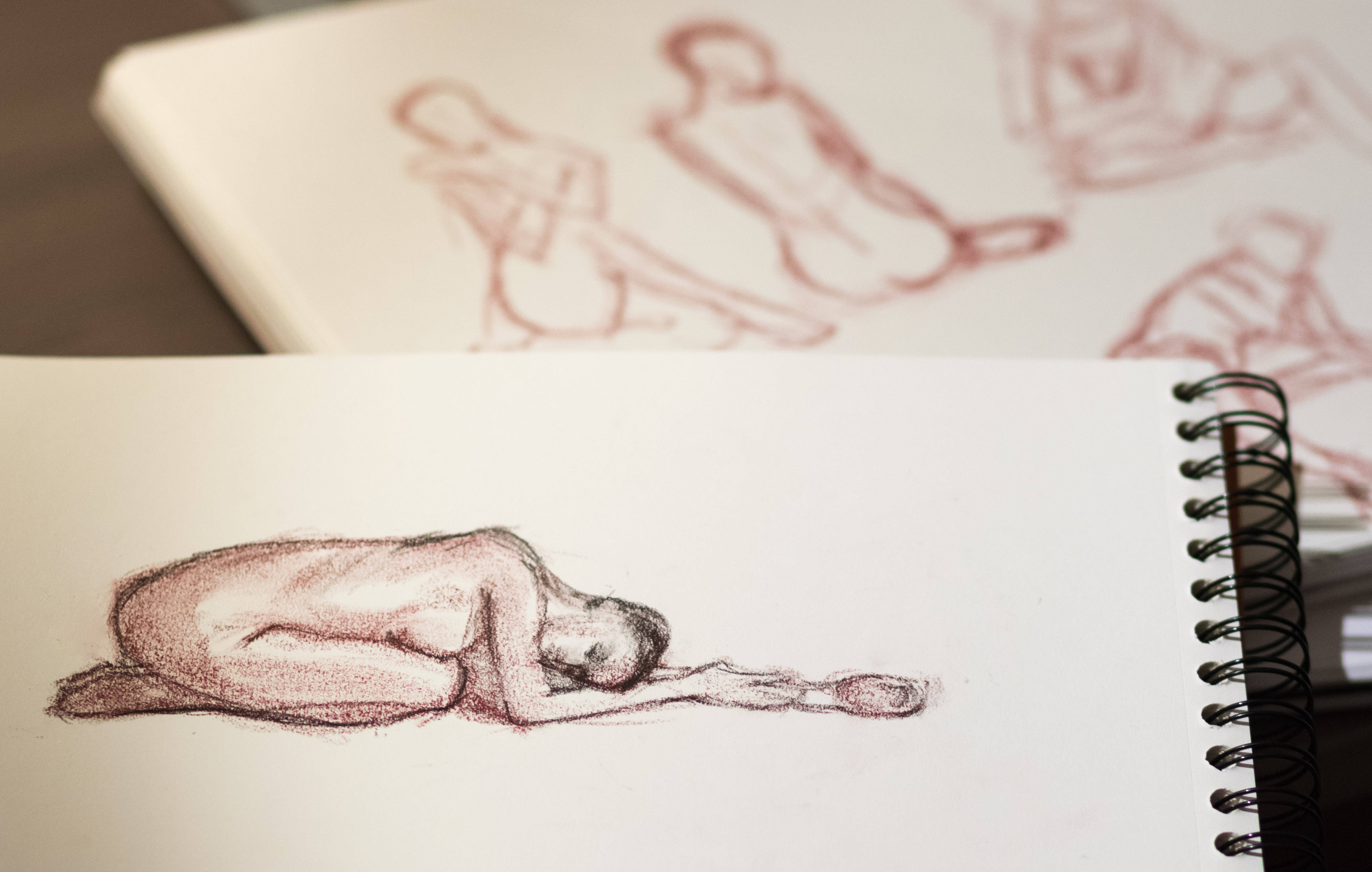 pencil 桌布 壁紙 — 在螺旋裝訂素描本頁面上，一幅詳細的紅色粉筆素描，描繪一個胎兒姿勢的裸體人物。