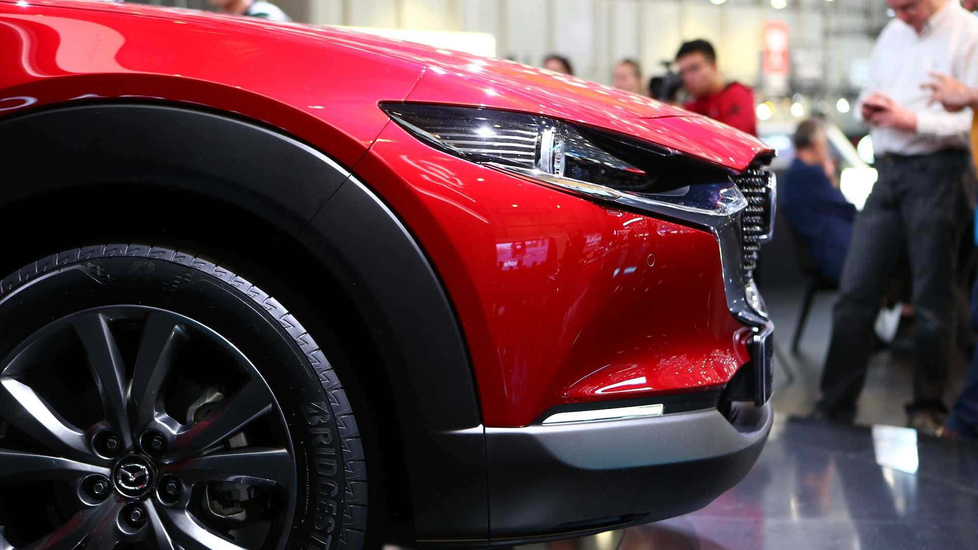 Mazda Cx-30 桌布 壁紙 — 在車展上，一輛亮紅色SUV的前擋泥板和車輪特寫，背景有模糊的與會者。