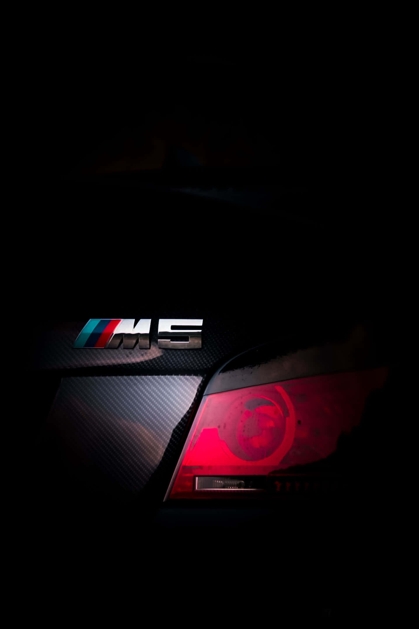 Bmw Android 桌布 壁紙 — 在近乎全黑的環境中，時尚的BMW M5徽章在碳纖維和鮮紅色尾燈的映襯下閃耀光芒。