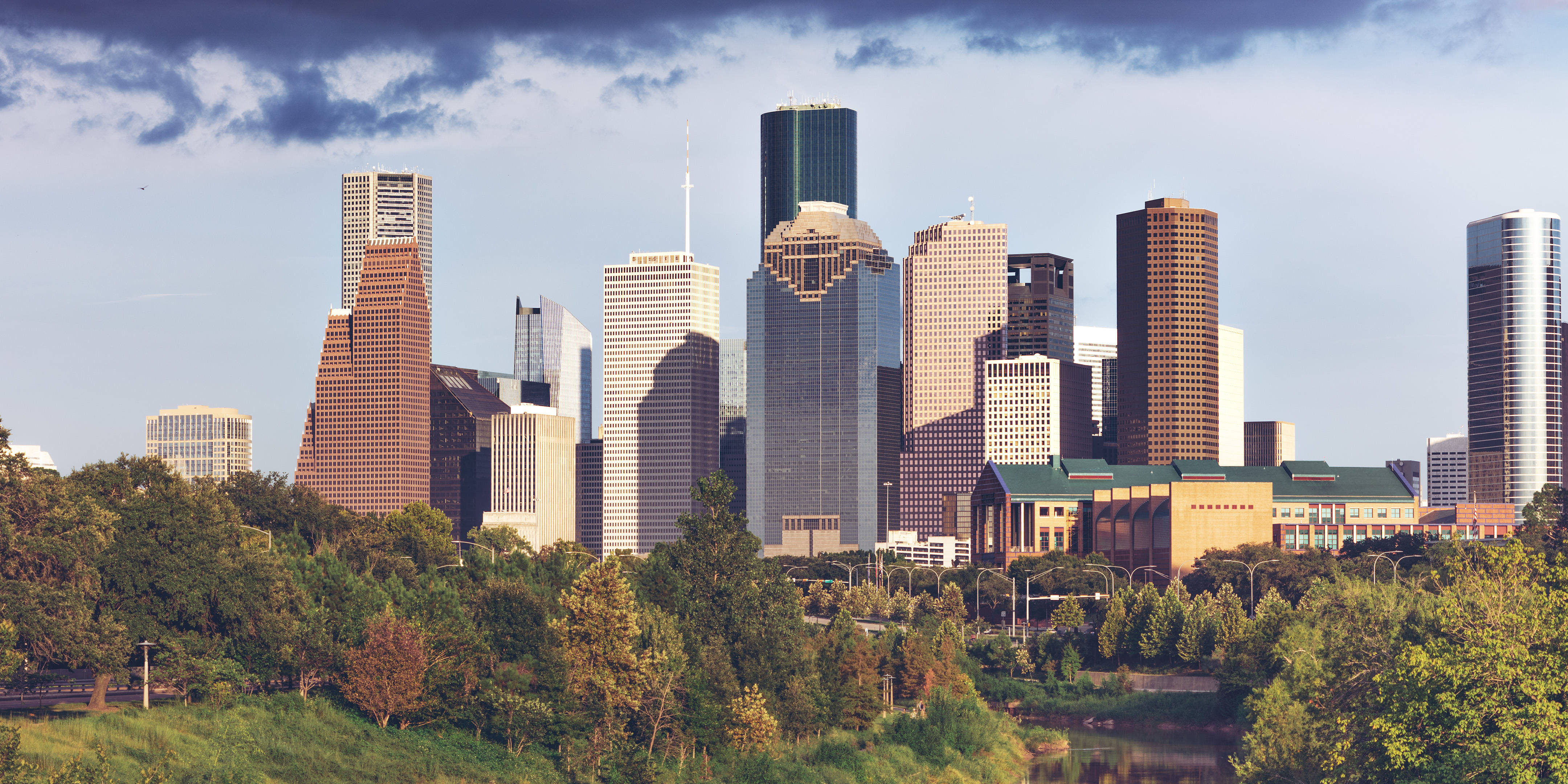 Houston 桌布 壁紙 — 在部分多雲的天空下，充滿活力的城市天際線，高聳的摩天大樓聳立在茂密的綠樹之上。