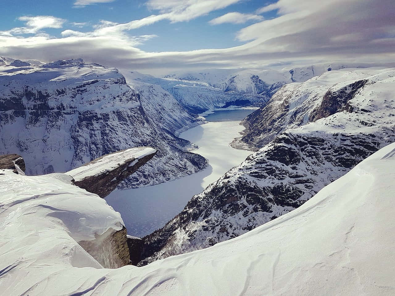 Winter Landscape 桌布 壁紙 — 在部分多雲的天空下，崎嶇山峰之間環抱著冰封峽灣的壯麗雪景。