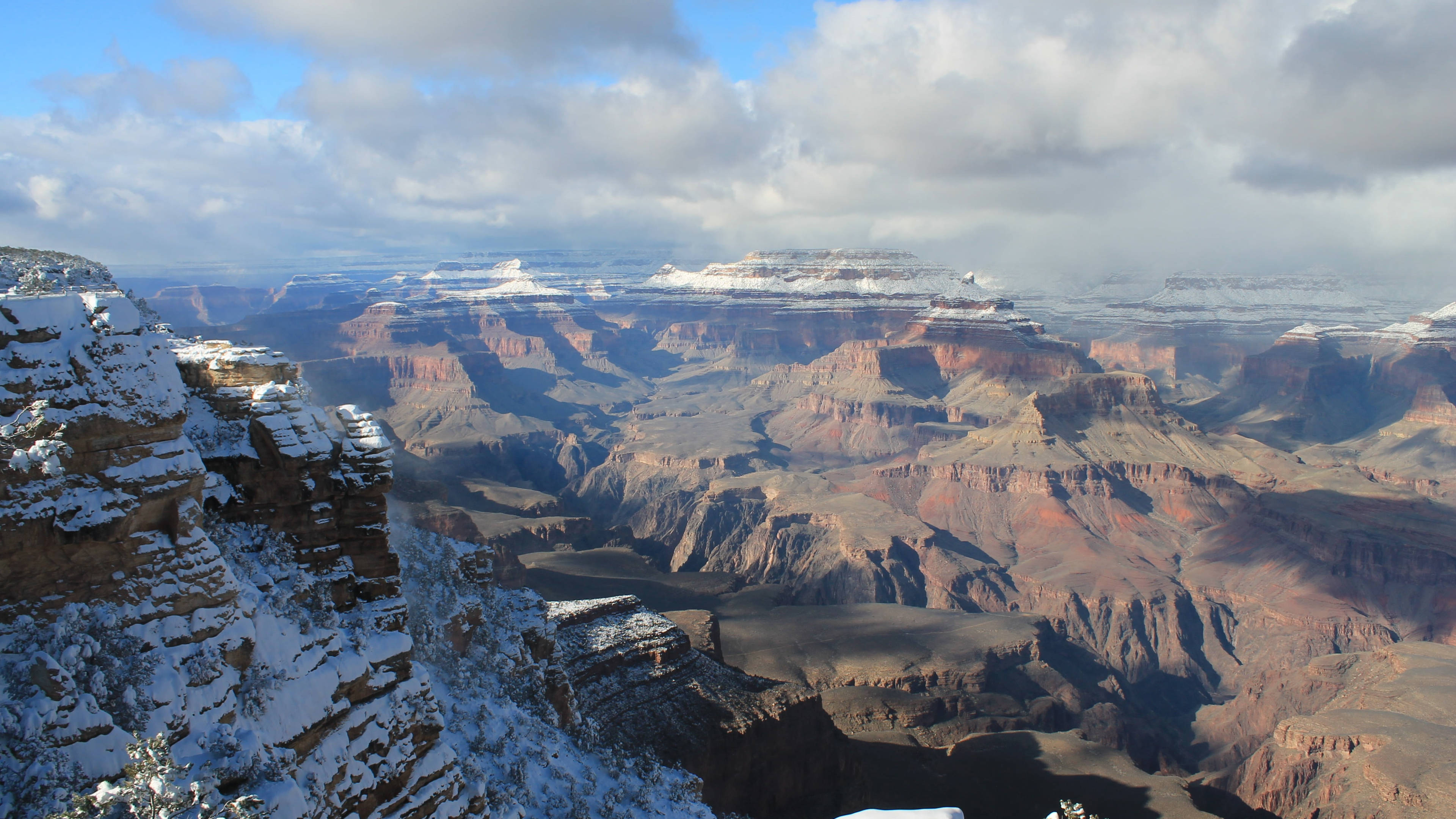 Canyon 桌布 壁紙 — 在部分多雲的天空下，白雪覆蓋了大峽谷崎嶇的懸崖和層層疊疊的峽谷。