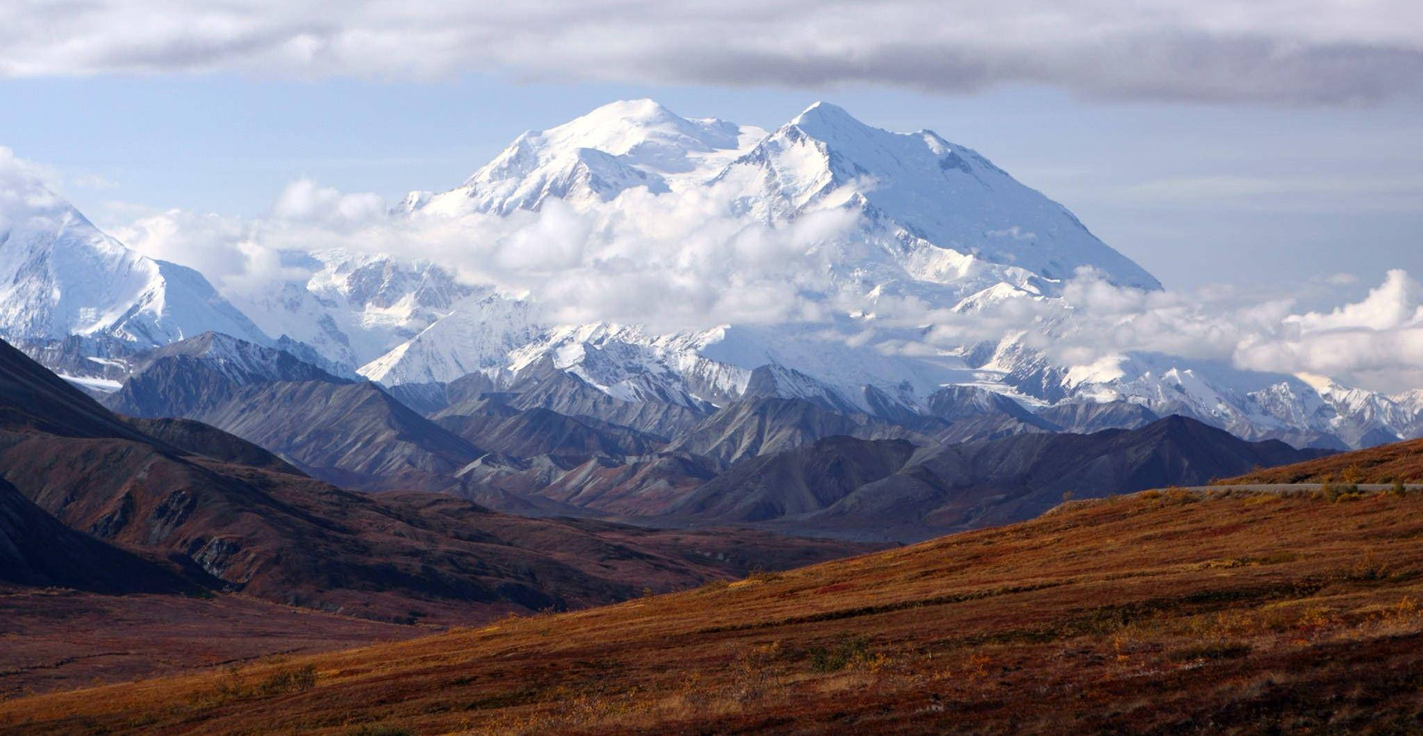 山脈 桌布 壁紙 — 在部分多雲的天空下，雄偉的雪山頂峰聳立在崎嶇的棕色山丘之上。