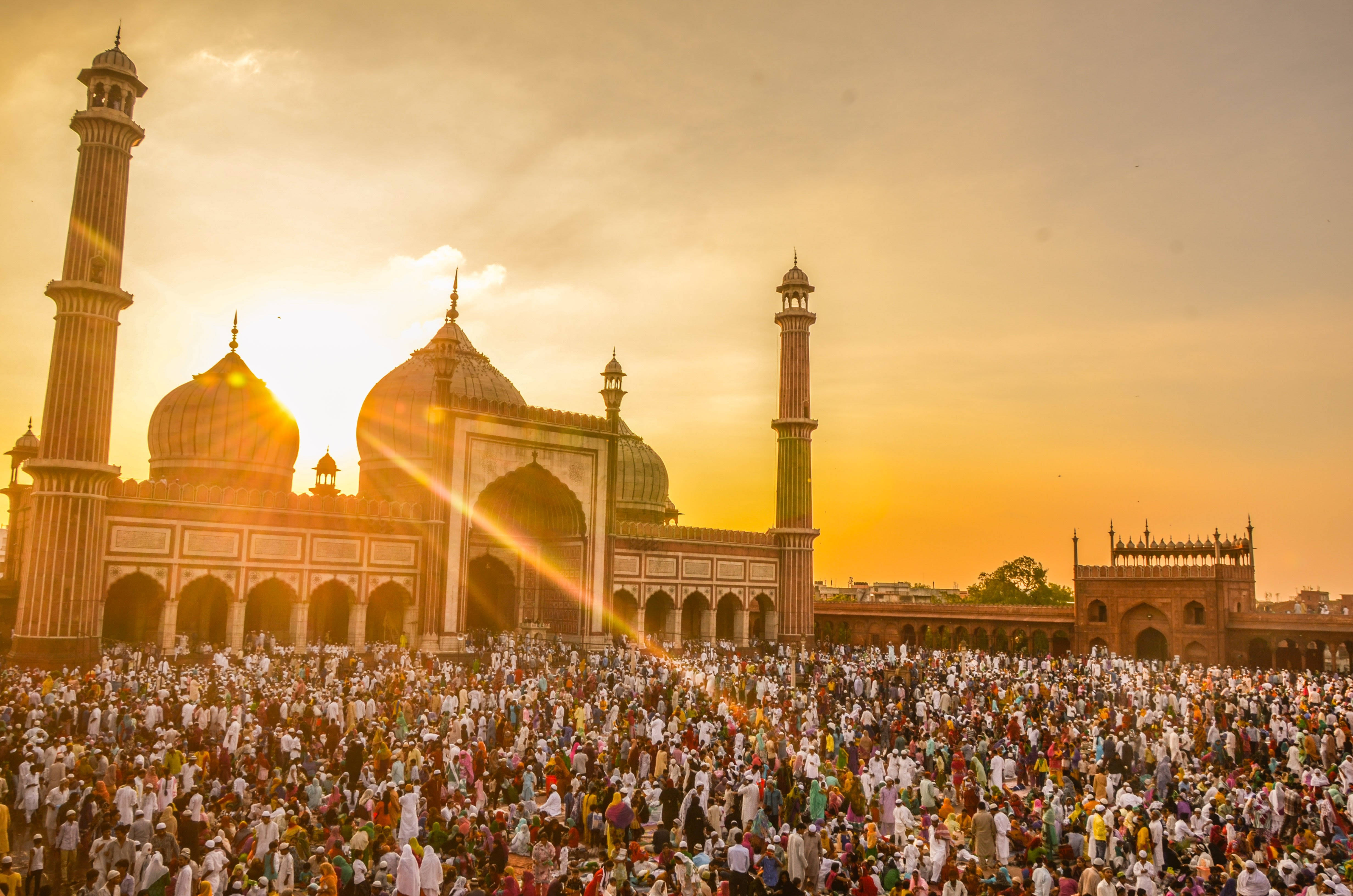 Best Islamic 桌布 壁紙 — 在金色日落時分，大量人群聚集在雄偉的賈瑪清真寺前，燦爛的陽光穿透雲層。