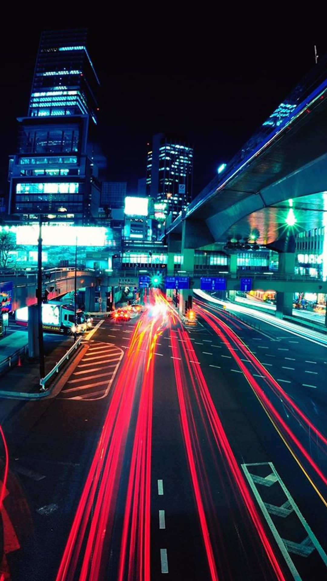 City iPhone 桌布 壁紙 — 在閃爍的摩天大樓和高架高速公路下，鮮紅色的光軌劃過繁華的城市街道夜景。