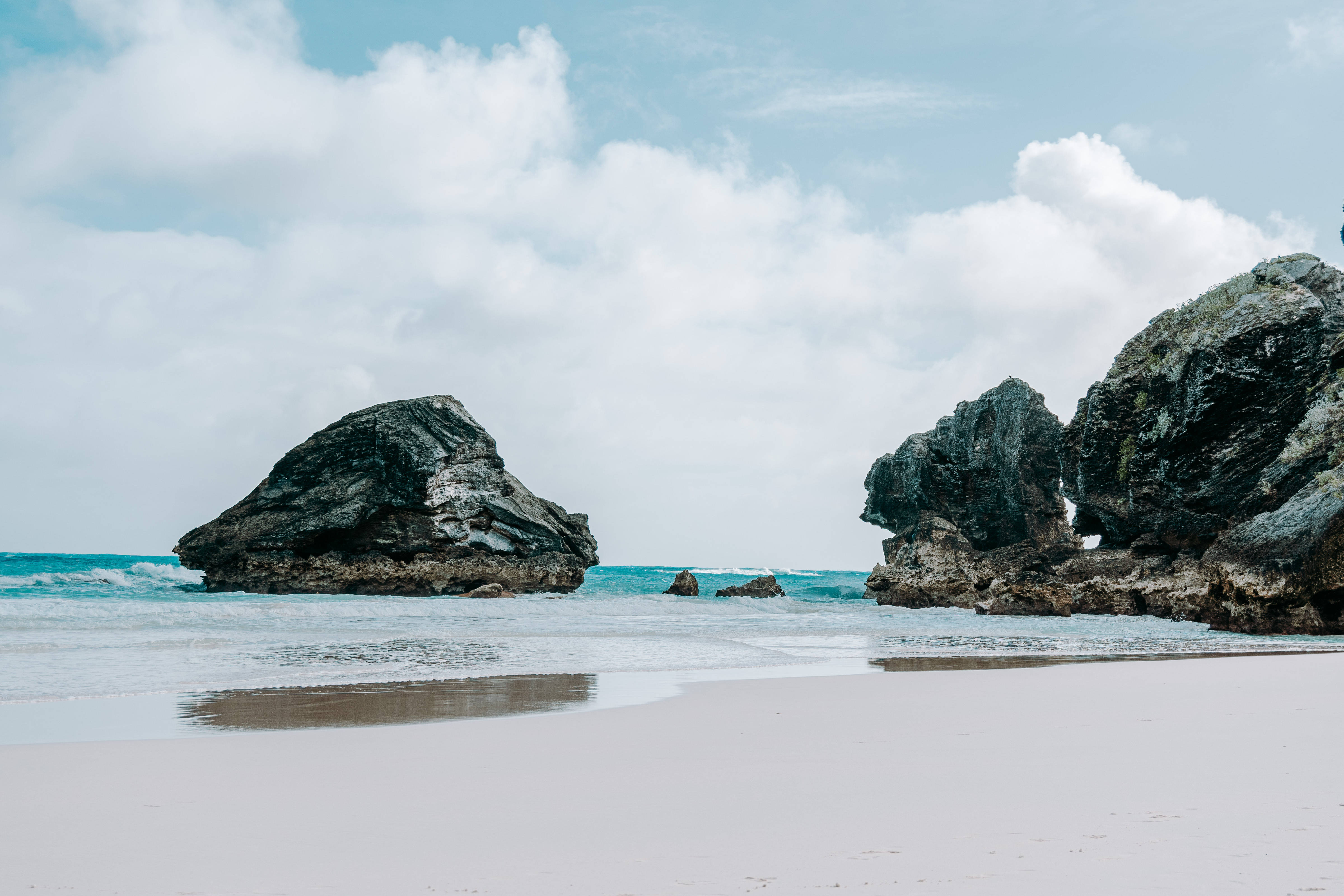 Bermuda 桌布 壁紙 — 在陰天之下，一個寧靜的海灘，有白沙和從碧綠海水中突出的大塊黑色岩石。