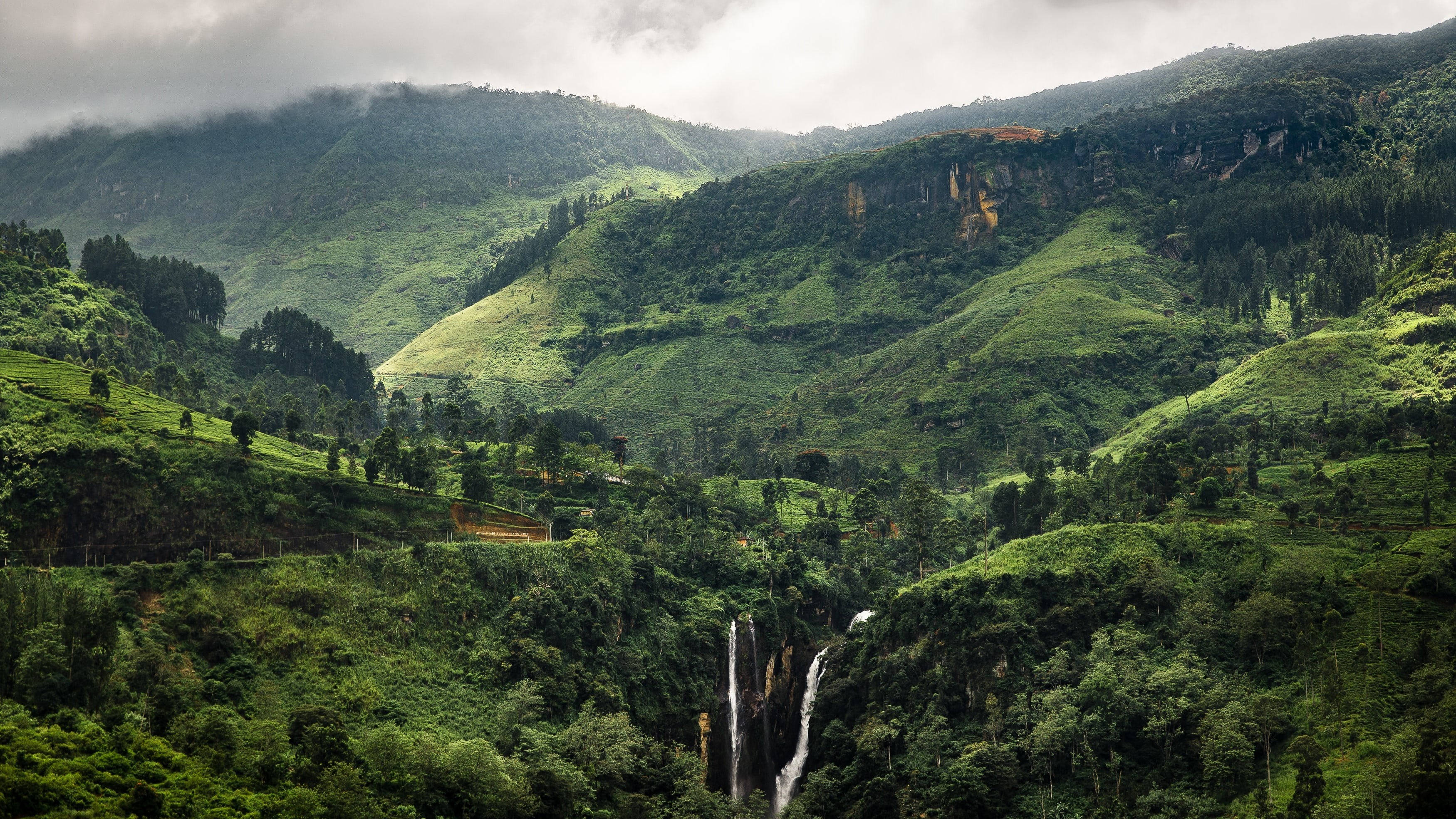 Sri Lanka 桌布 壁紙 — 在陰天之下，一道雄偉的瀑布穿過鬱鬱蔥蔥的綠色山脈傾瀉而下。