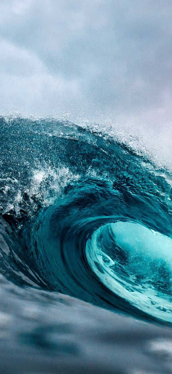Surfing iPhone 桌布 壁紙 — 在陰天之下，一道高聳的藍綠色海浪捲成完美的筒狀。