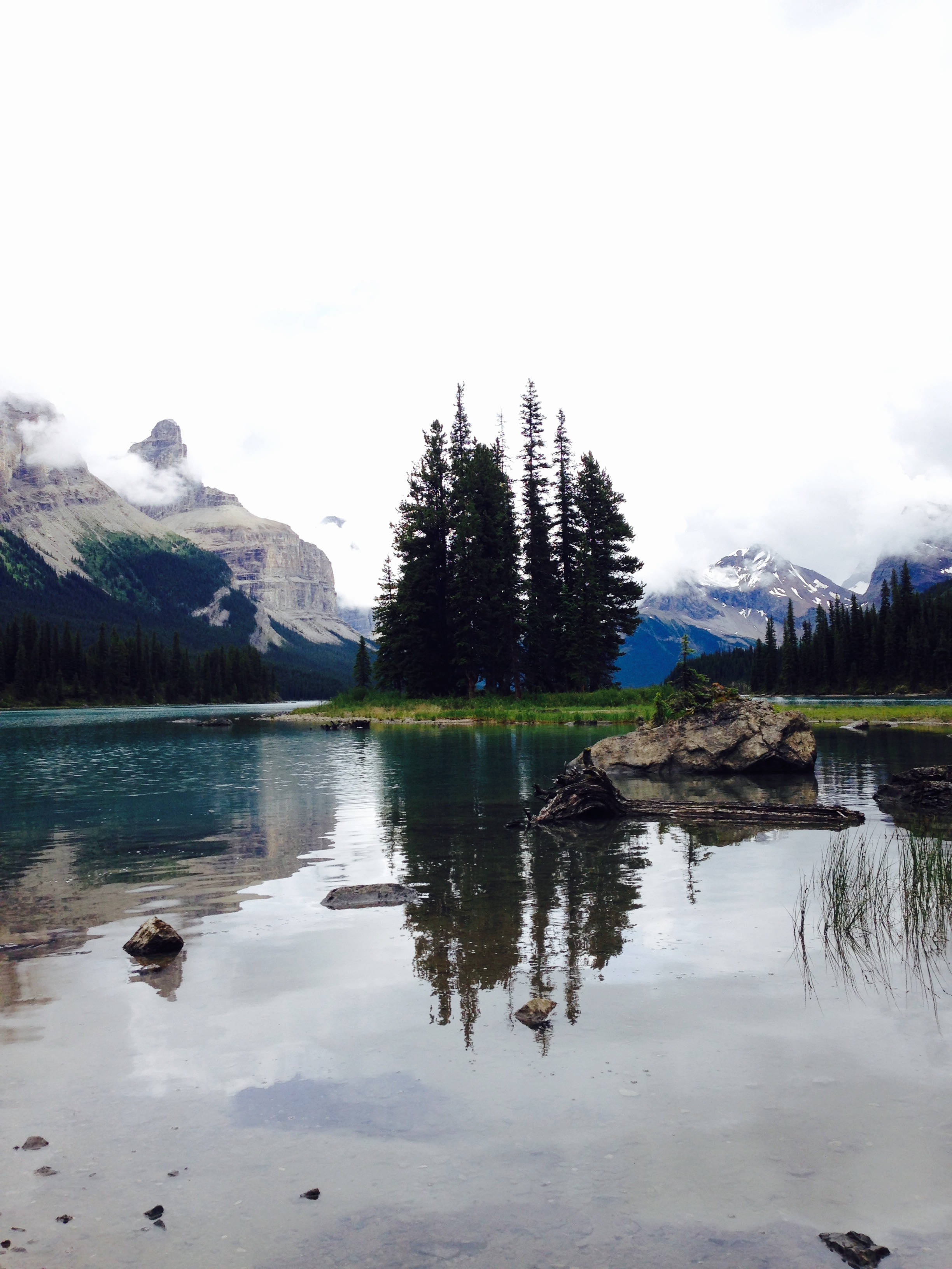 canada iPhone 桌布 壁紙 — 在陰天之下，寧靜的山湖映照著高聳的山峰和常綠樹木。