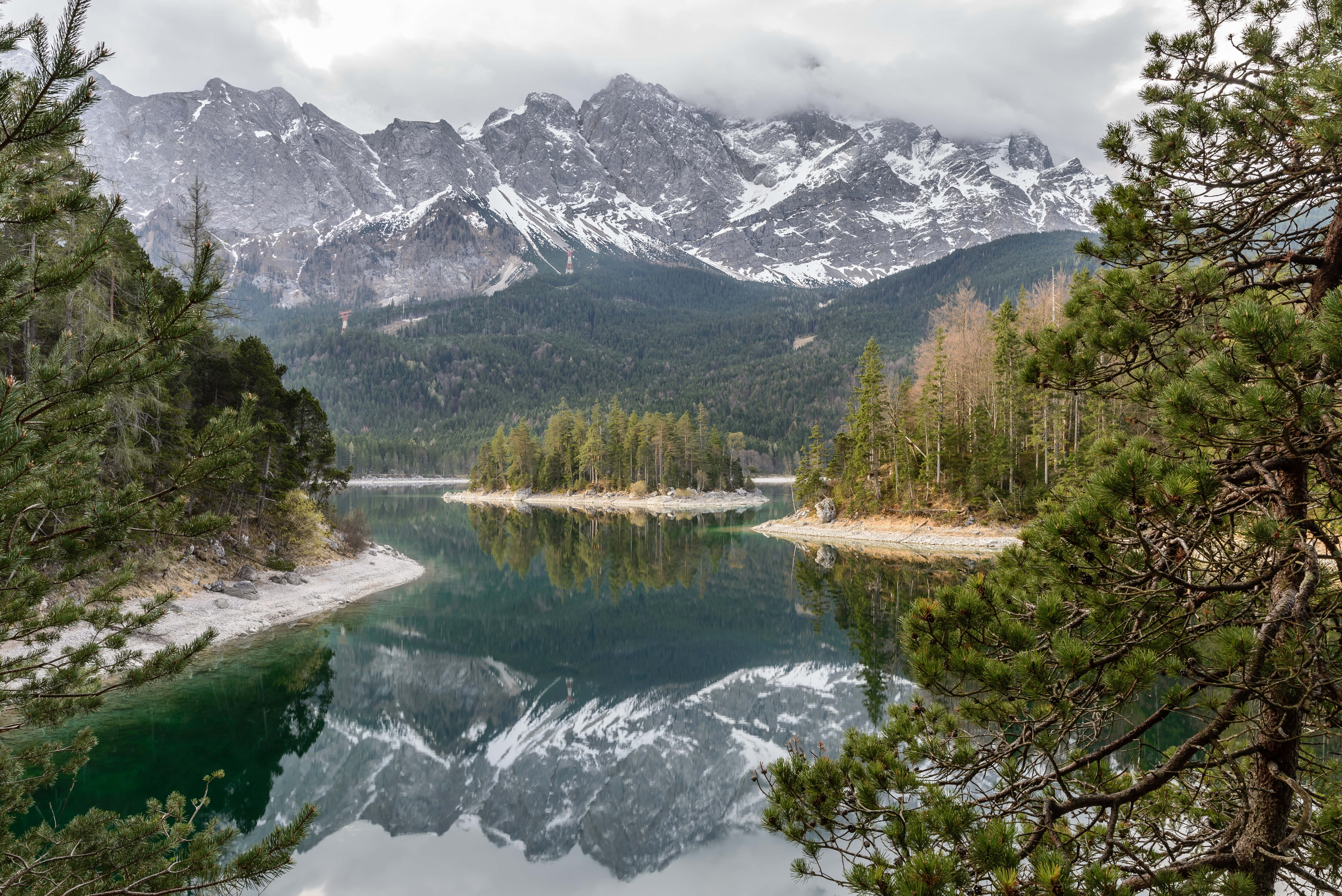 Beautiful Mountain Lake 桌布 壁紙 — 在陰天之下，寧靜的高山湖泊倒映著積雪的山峰和常綠樹木。