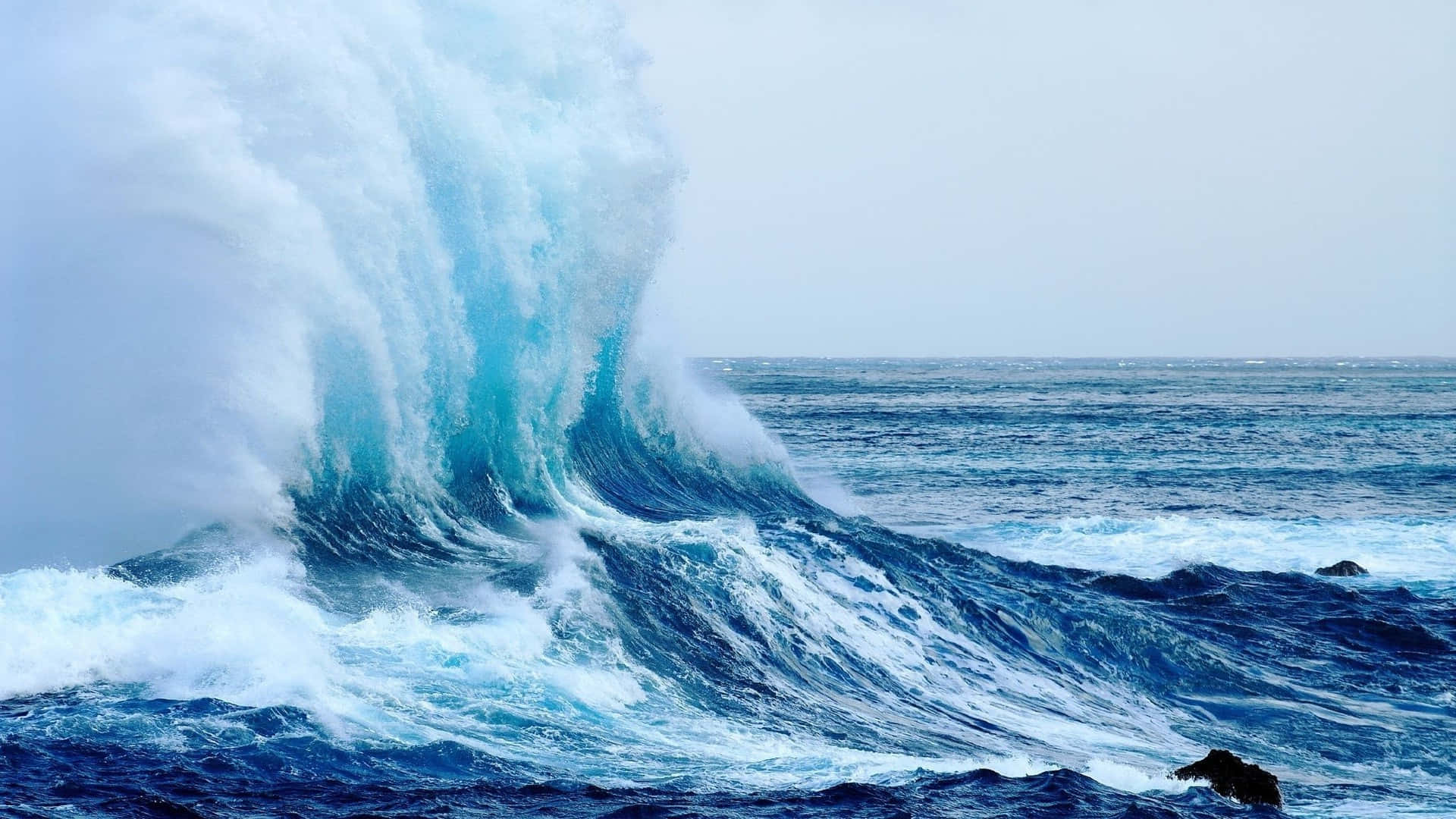 Wave 桌布 壁紙 — 在陰天之下，巨大的藍綠色波浪帶著白色泡沫沖擊著深色岩石。