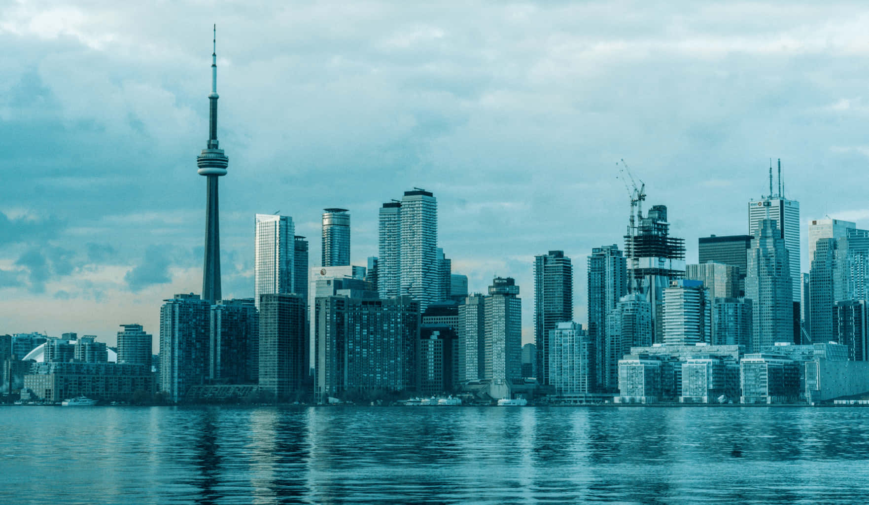Toronto Skyline 桌布 壁紙 — 在陰天之下，平靜水面上倒映著帶有青綠色調的城市天際線，包括CN塔和現代摩天大樓。