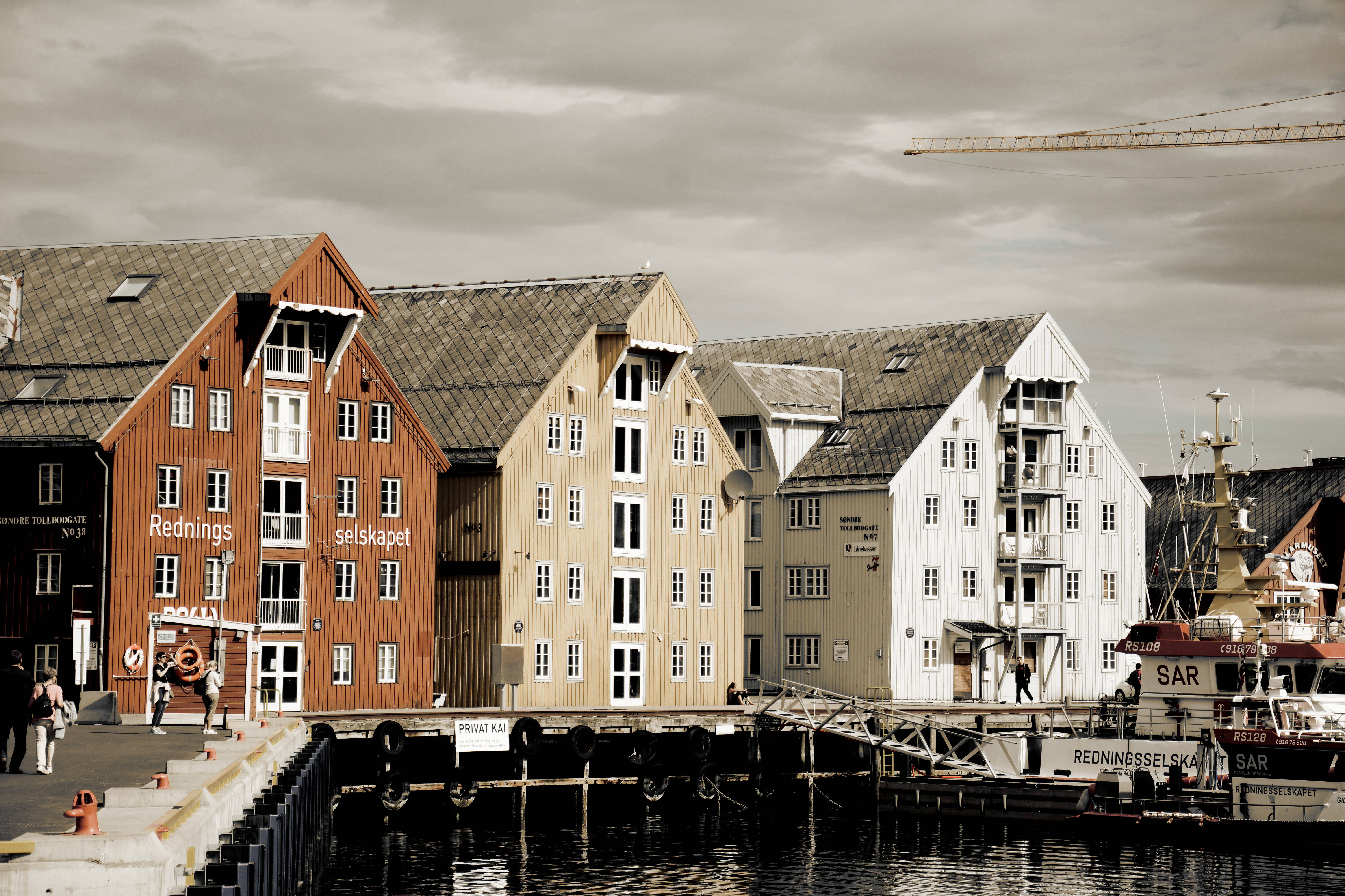 Norway 桌布 壁紙 — 在陰天之下，平靜的港灣旁排列著紅色、米色和白色外牆的復古木質海濱建築。