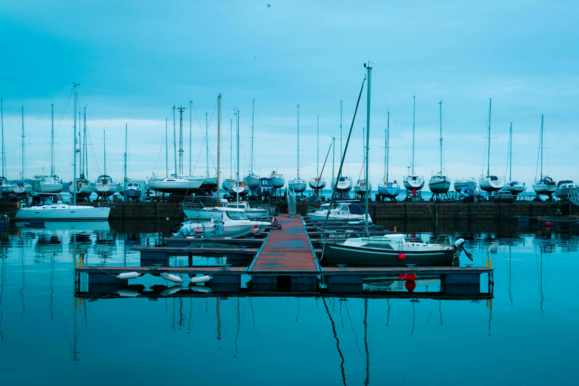 Marina, harbor, yachts, boats, dock, pier, calm water, waterfront, sea, nautical, travel, tourism 壁紙 — 在陰天之下，平靜的藍綠色海水中停泊著帆船的寧靜碼頭。