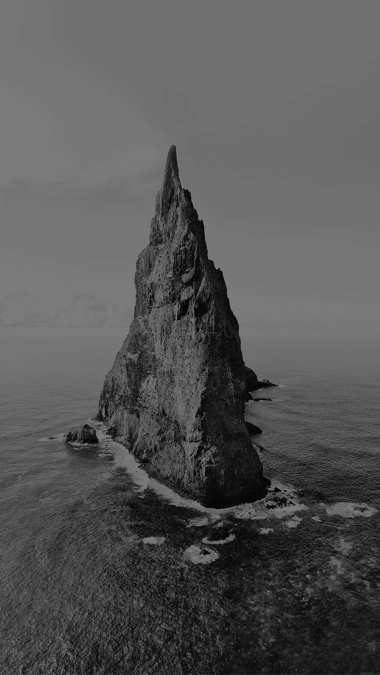 Dark Island 桌布 壁紙 — 在陰天之下，從湍急海洋中聳立的海蝕柱的鮮明黑白空拍圖。