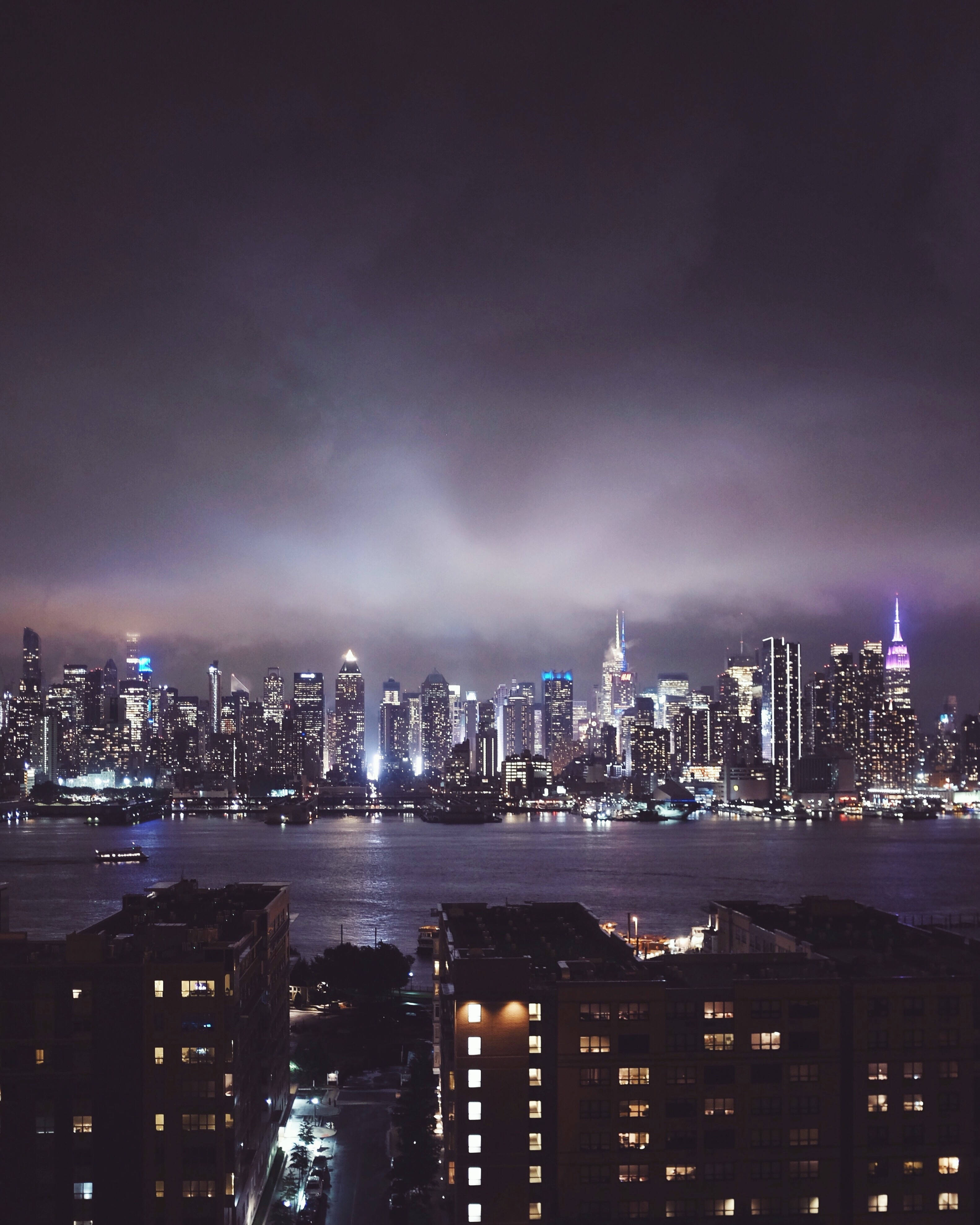 Nyc 桌布 壁紙 — 在陰天之下，紐約市璀璨的天際線倒映在黑暗水中的戲劇性夜景。