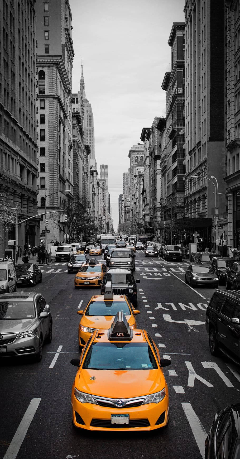 Road 桌布 壁紙 — 在陰天之下，鮮黃色的計程車帶領車流穿過紐約市一條狹窄的街道，兩旁是高聳的歷史建築。