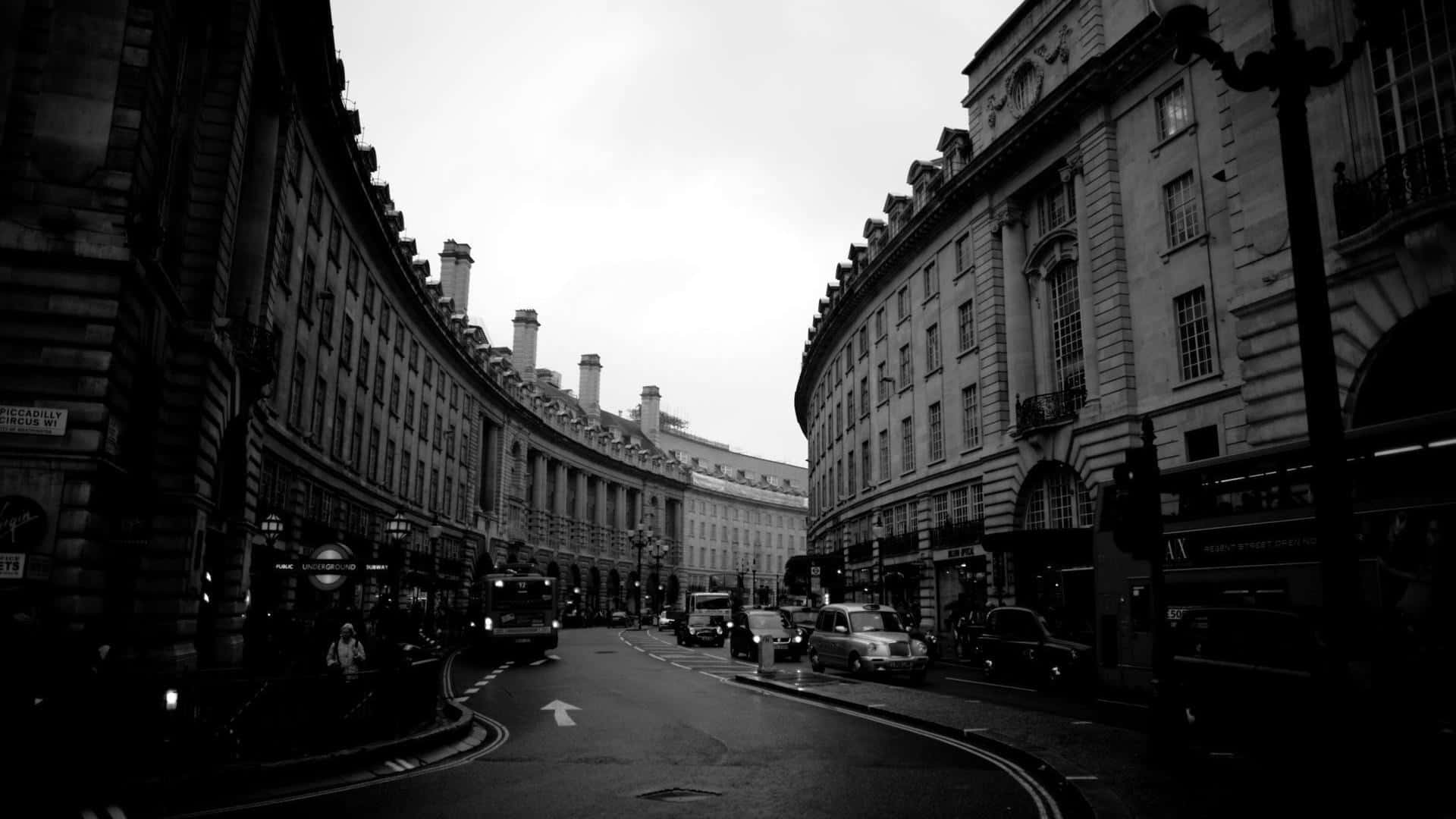 Black And White Street 桌布 壁紙 — 在陰天天空下，一條彎曲的歷史街道兩旁排列著宏偉的石建築和復古汽車的單色景觀。